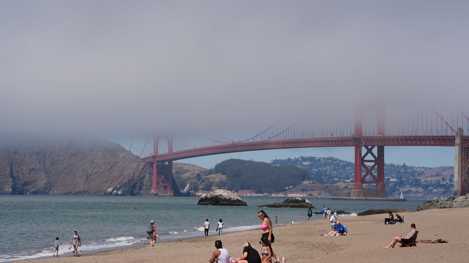 People on a beach in San Francisco, with the Golden Gate Bridge in the background covered in fog. 
