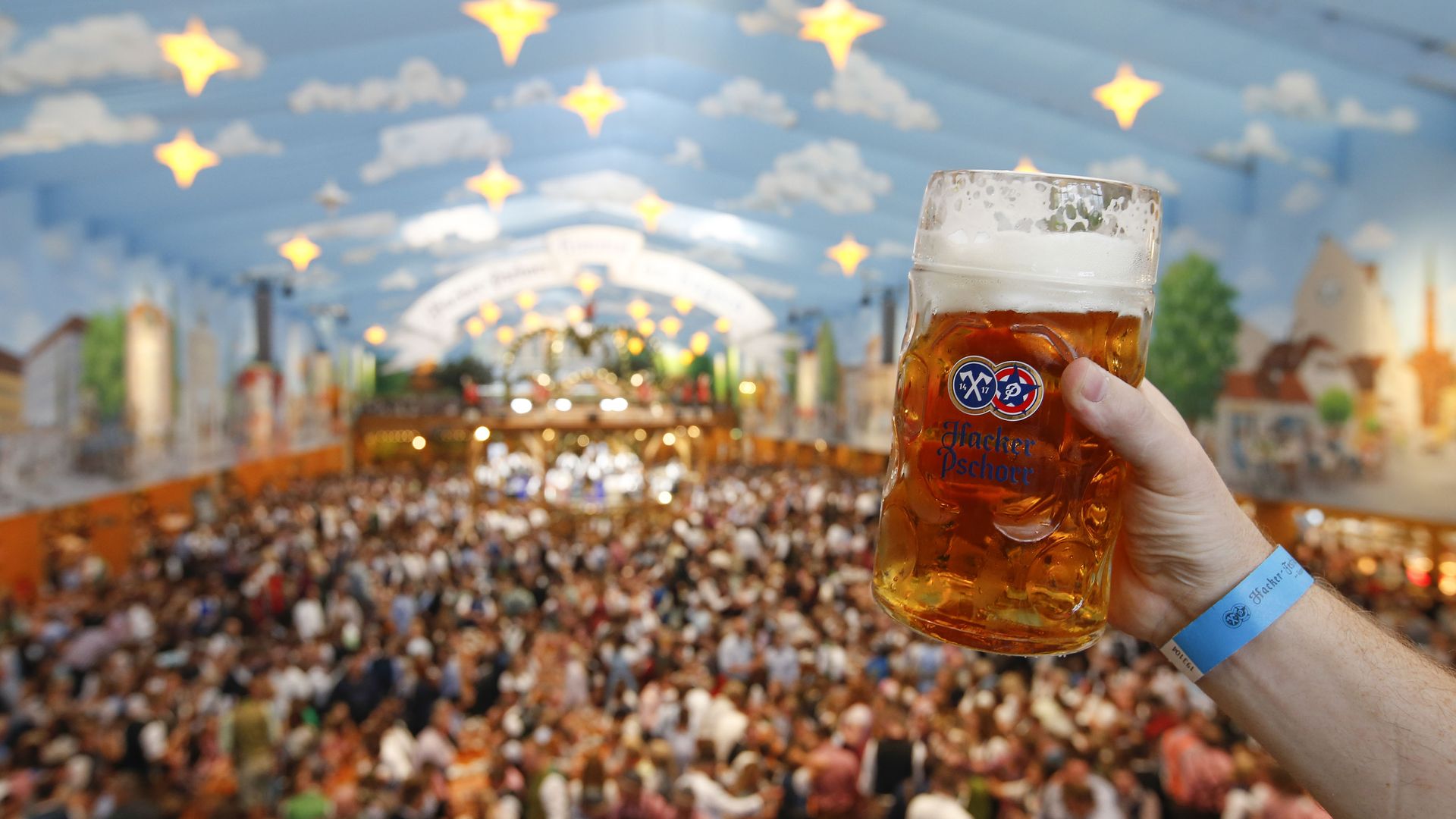 A person holding a large mug of beer in front of a giant crowd celebrating Oktoberfest.