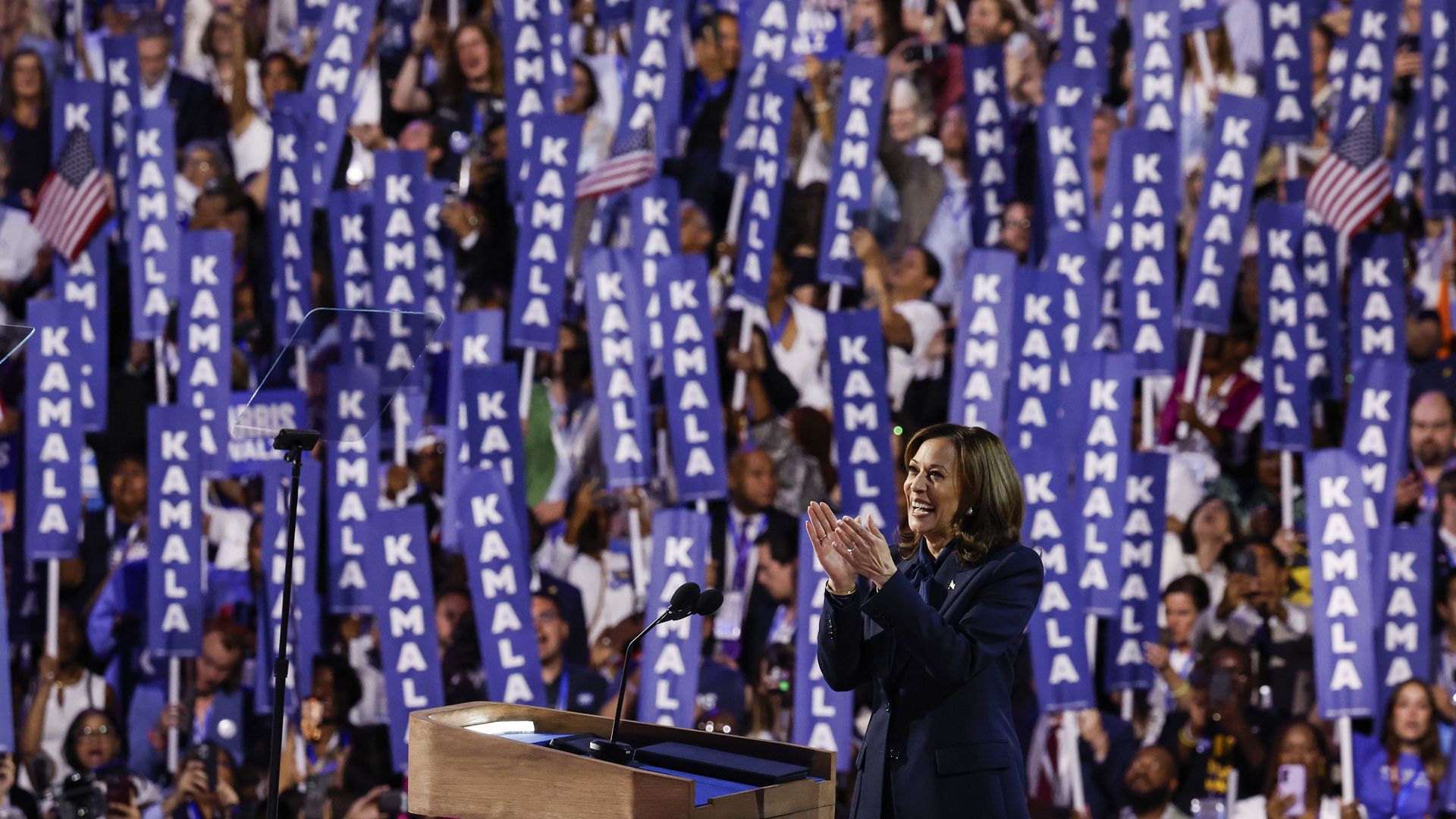 Vice President Harris cheers at the DNC while supporters hold "Kamala" signs.