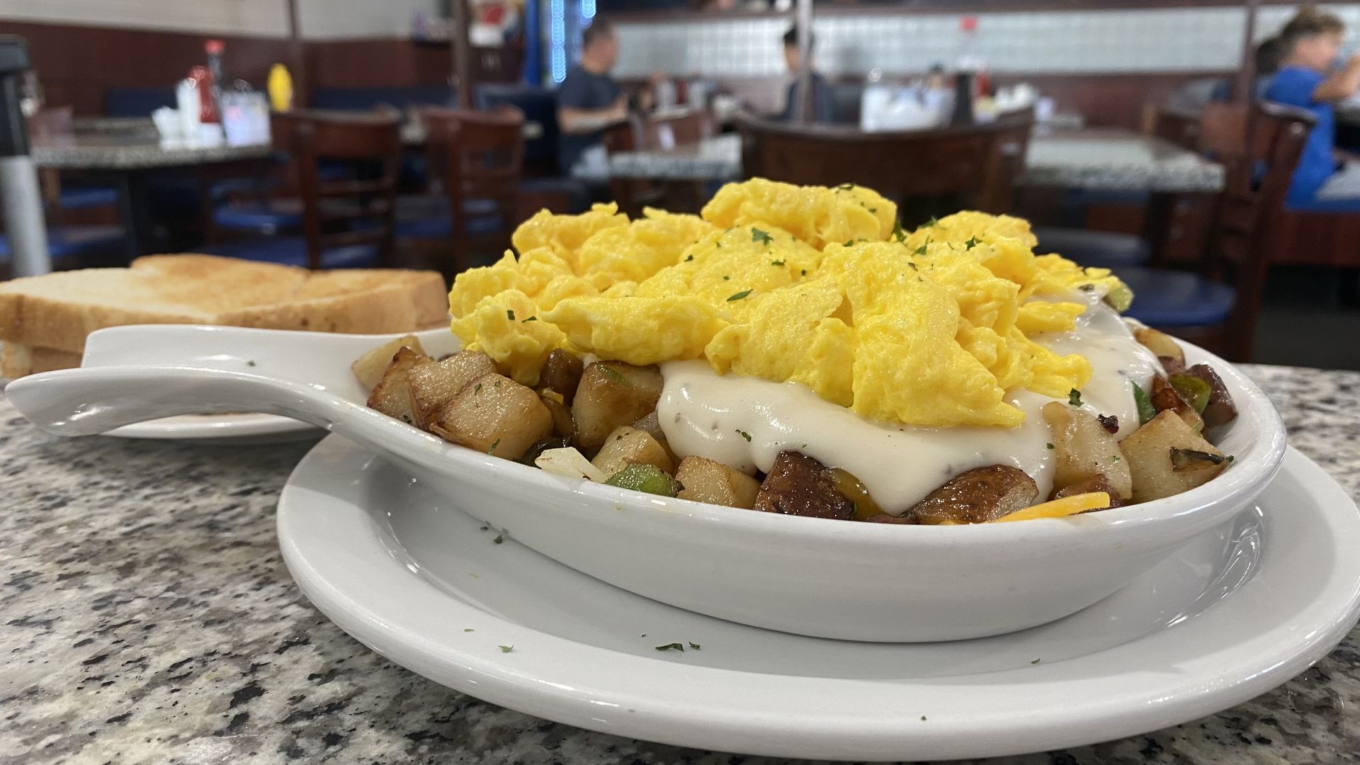 A skillet dish with scrambled eggs sitting on top of gravy, potatoes and veggies.