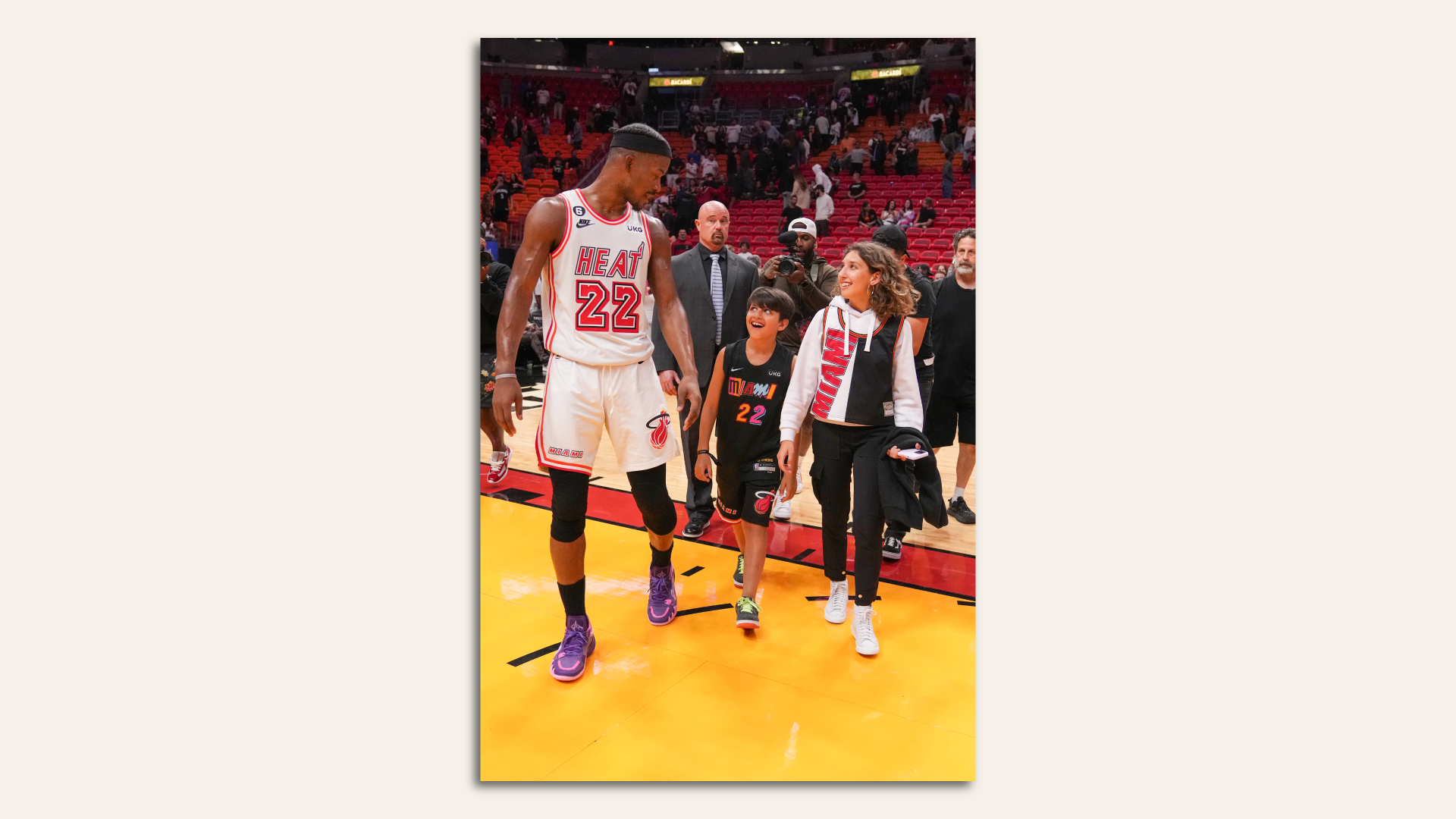 Miami Heat player Jimmy Butler walks with two fans on the court after a game.