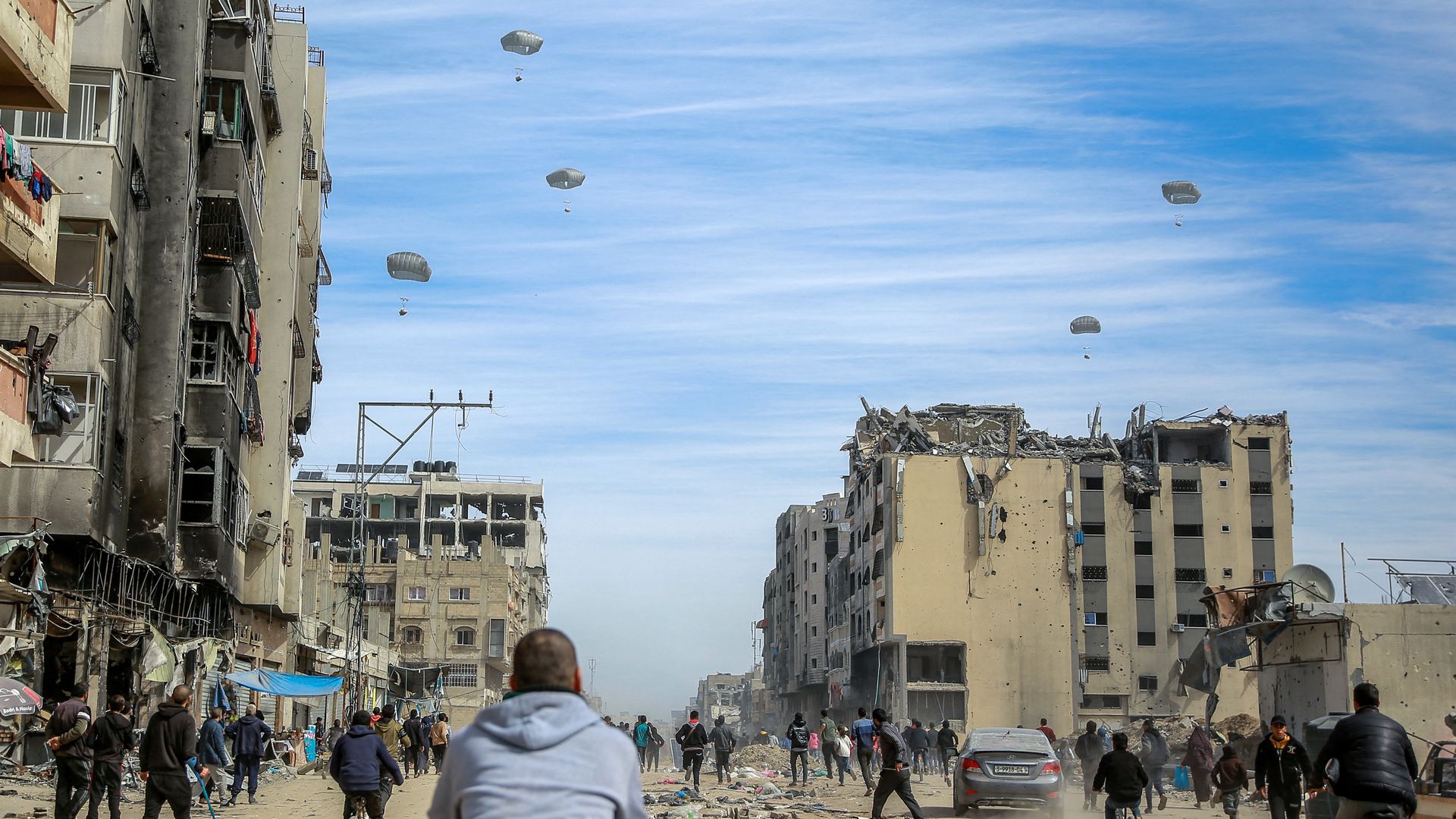 Palestinians run along a street as humanitarian aid is airdropped in Gaza City.