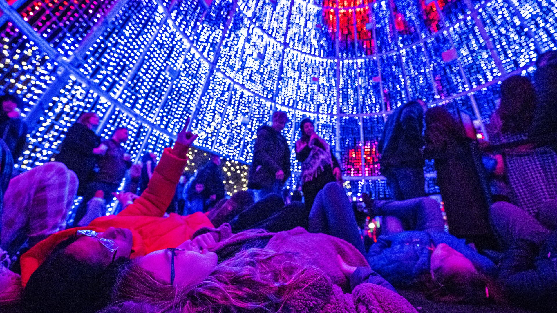 People lying on the floor and standing inside a dome-shaped structure filled with bright LED lights.
