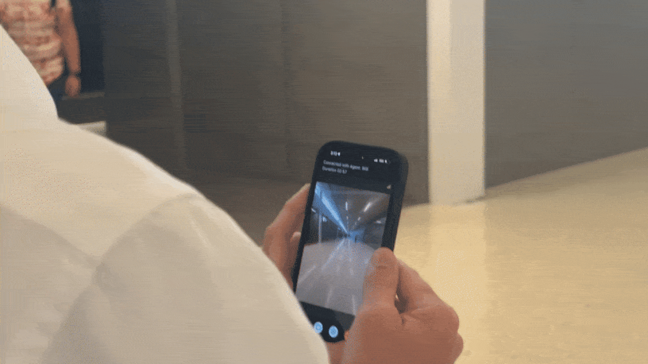 Person wearing a white shirt holding a phone, capturing a photo of an empty indoor corridor with shiny floors and ceiling lights reflected on the ground.