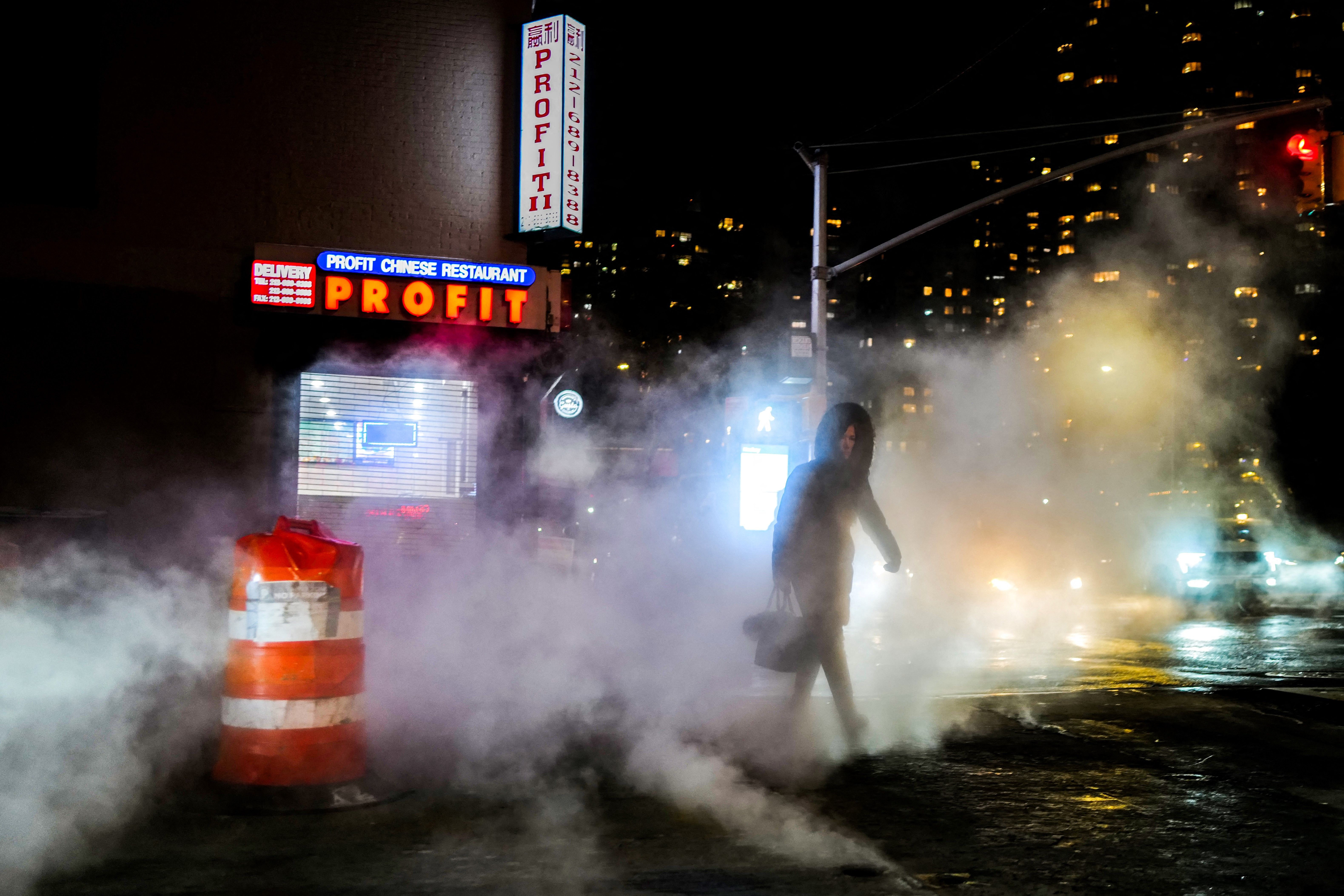 A woman crosses a street during a cold evening as hot steam escapes from the ground in the Manhattan borough of New York on January 16, 2024. New York finally ended a record streak of more than 700 days without measurable snowfall, with a thin layer of white powder covering Central Park and other parts of America's most populous city. 