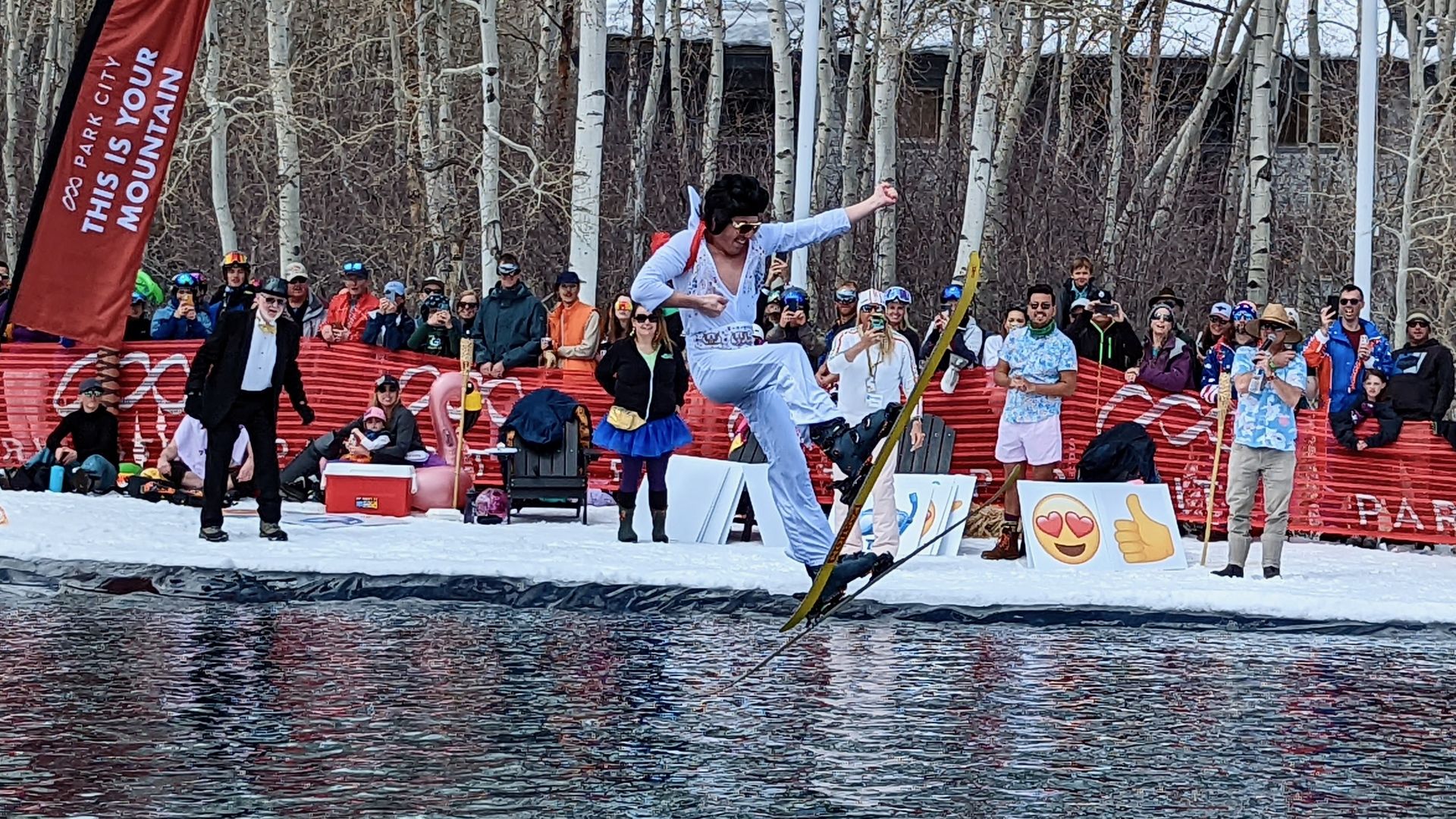 A man dressed as Elvis Presley plays air guitar during a ski jump over water.
