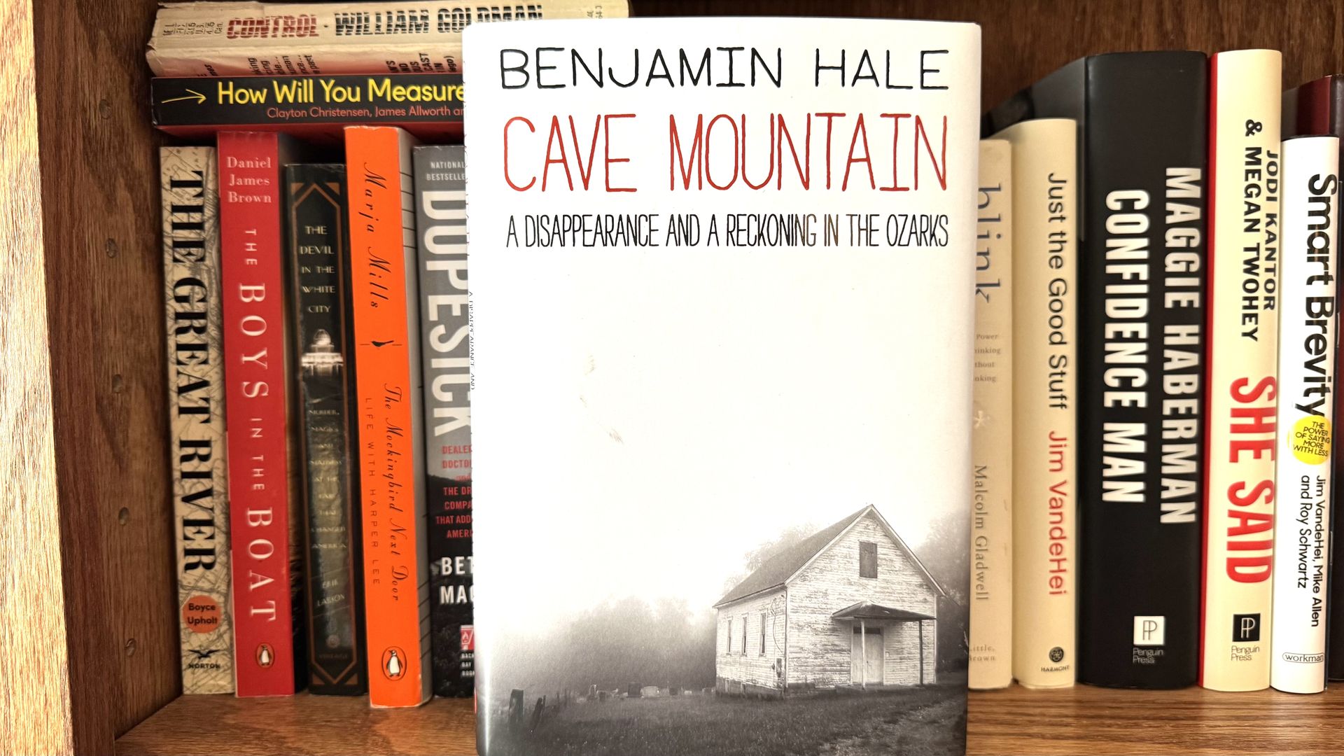 Book cover of Cave Mountain by Benjamin Hale displayed on a shelf, showing a small white church in a foggy landscape.
