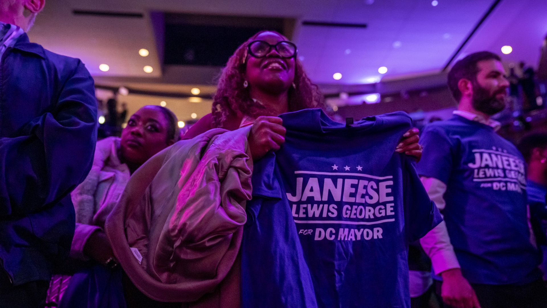 Inside Howard Theatre, a woman holds a purple t-shirt that says "Janeese Lewis George for DC mayor."