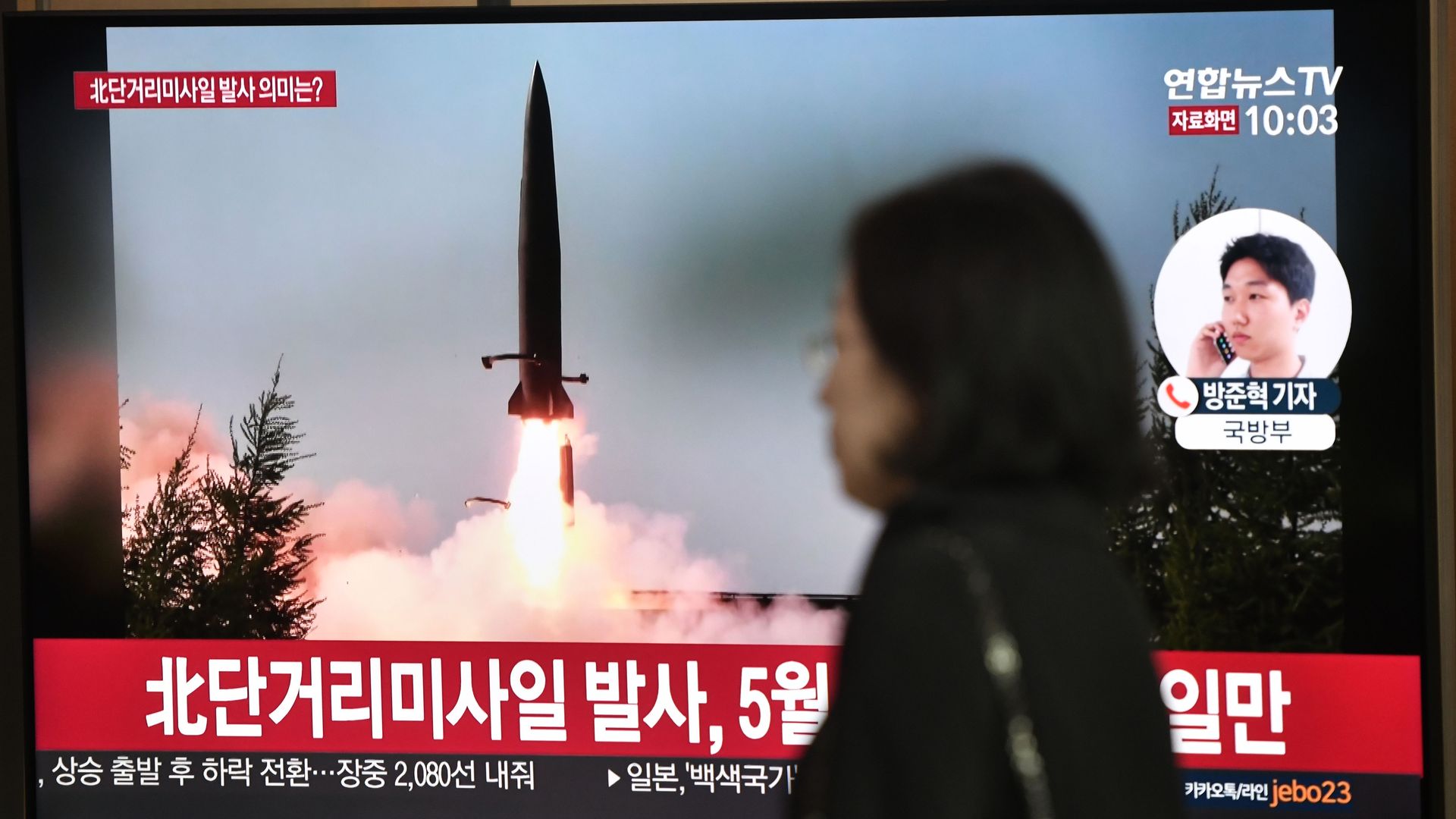 woman standing next to a television showing a missile launch