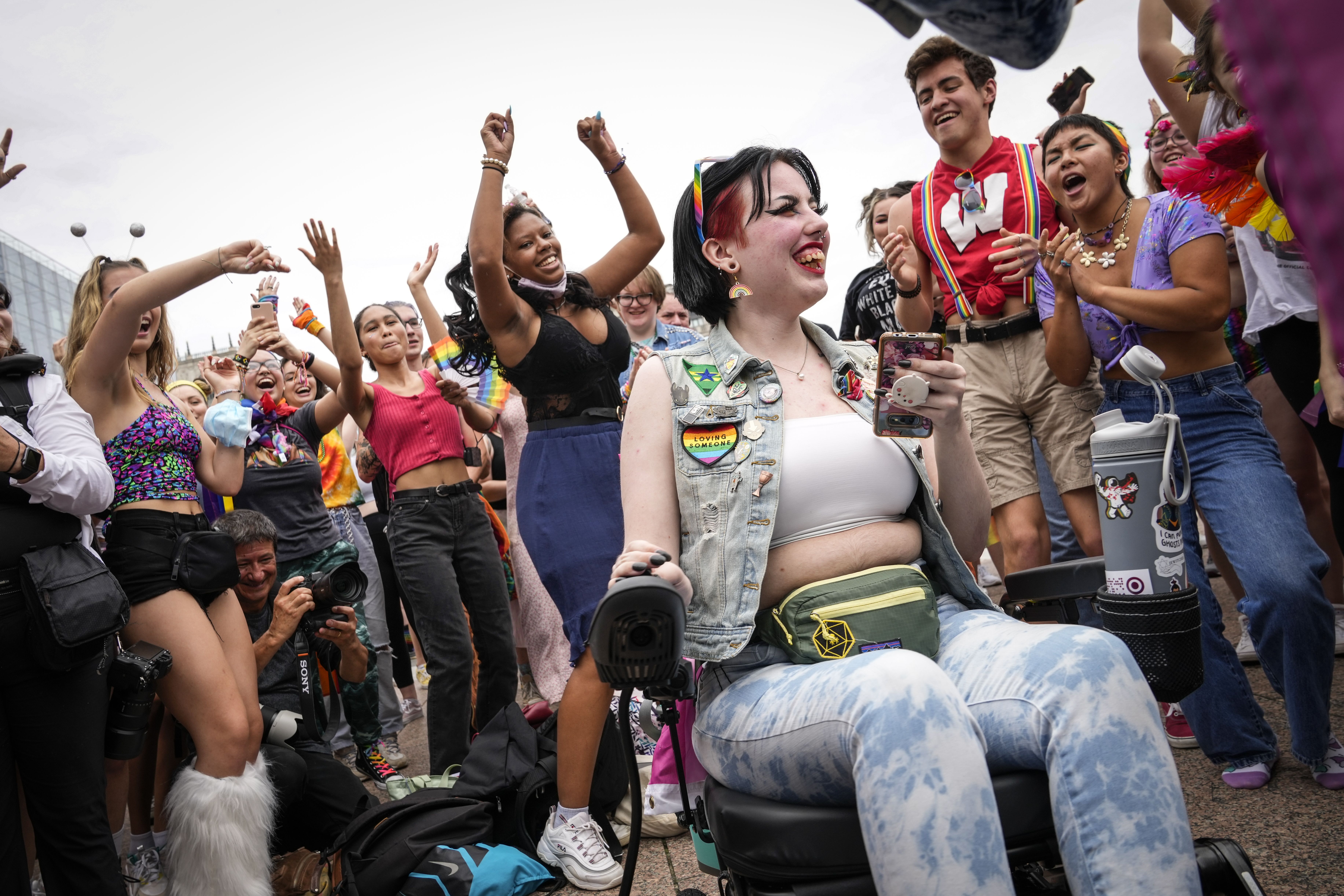 Photo of a person in a power wheelchair smiling as people around them cheer