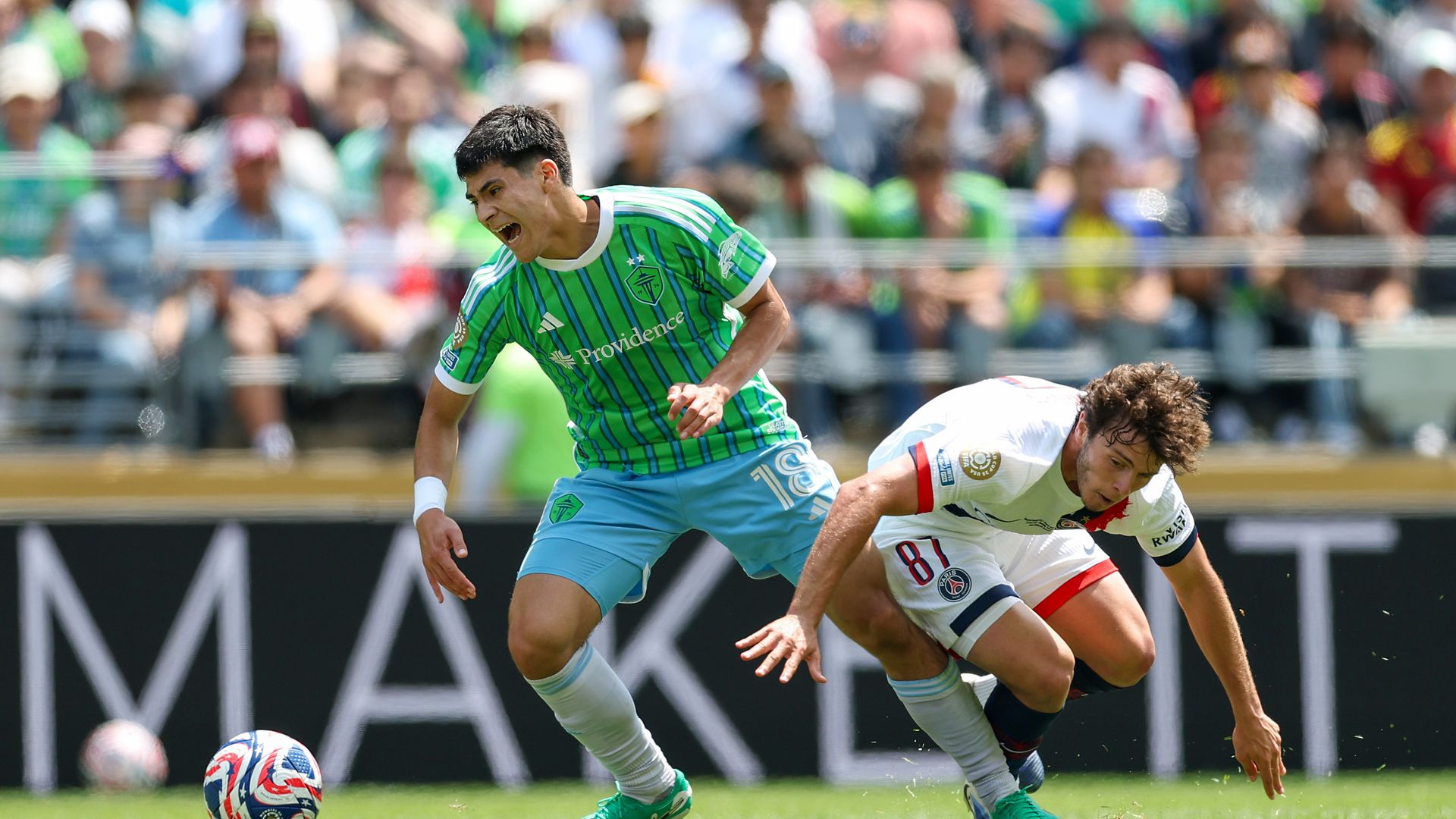 A Seattle Sounders FC player in green turns with the ball whilst under pressure from Paris Saint-Germain during a FIFA Club World Cup 2025 match at Lumen Field in Seattle. 