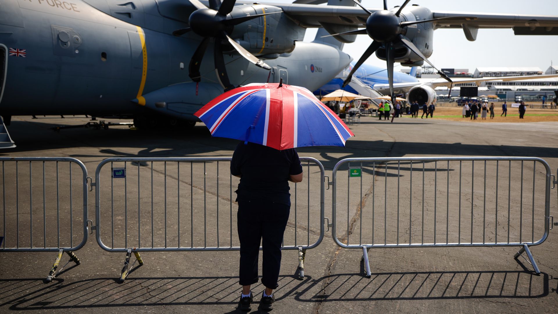 An attendee shelters from the sun under a Union Jack umbrella, during a heatwave, on the opening day of the Farnborough International Airshow in Farnborough, UK, on Monday, July 18, 2022.