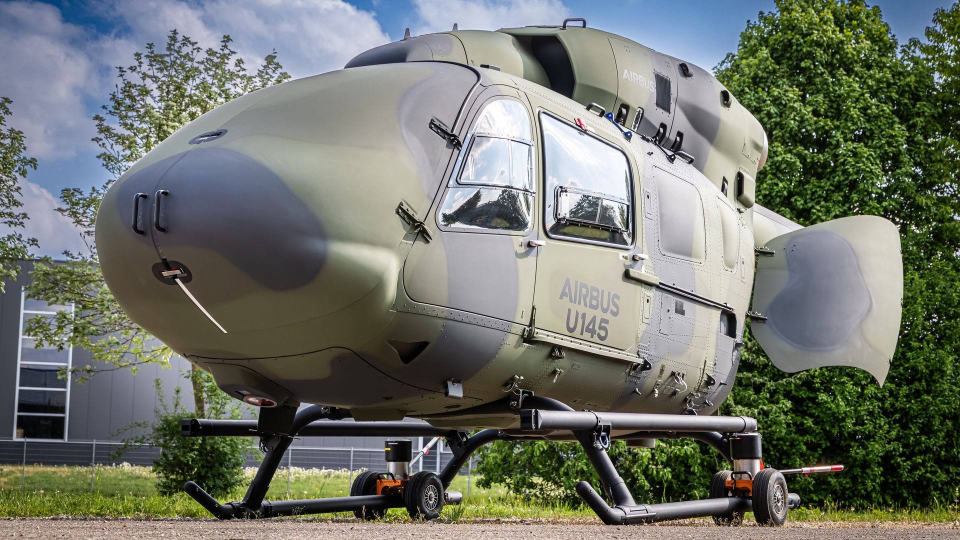 Close-up of a military-style helicopter in gray-green camo, labeled AIRBUS U145, with large cockpit windows and landing gear.