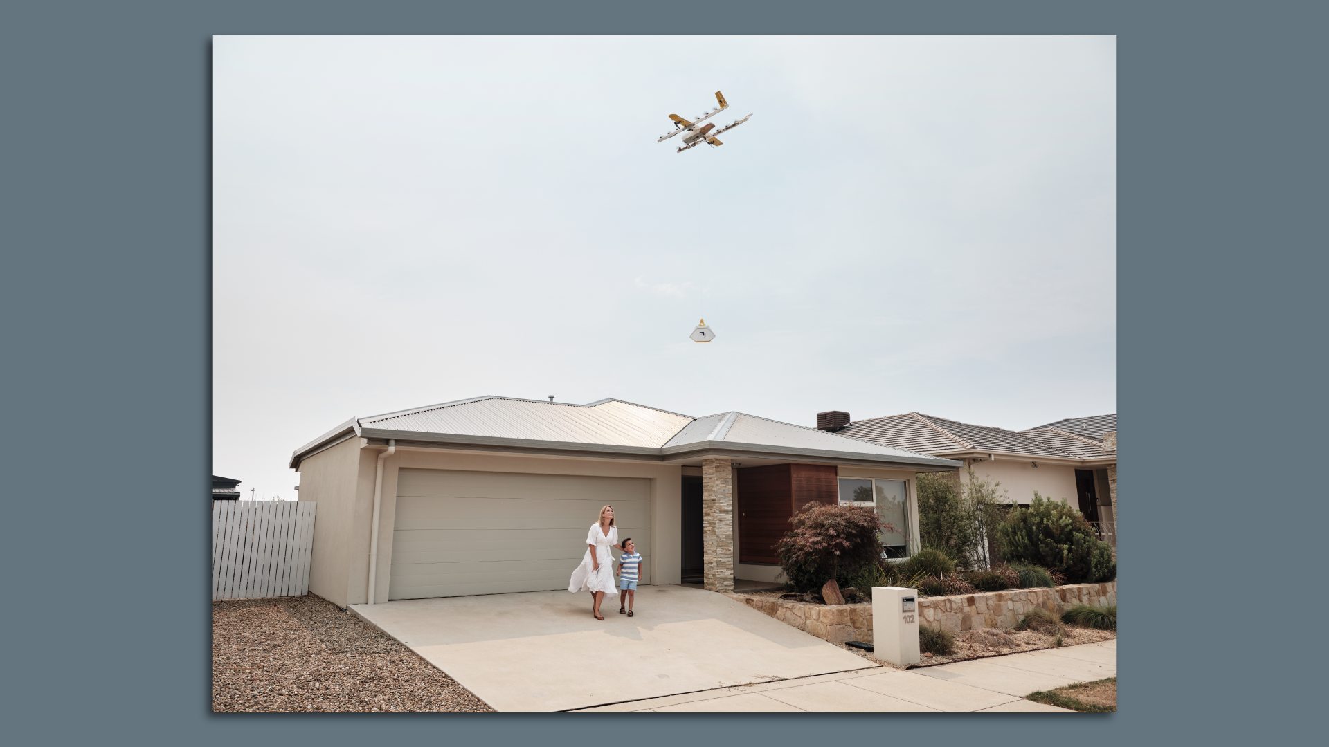 Image of a mother and son in the driveway, watching a drone delivery.
