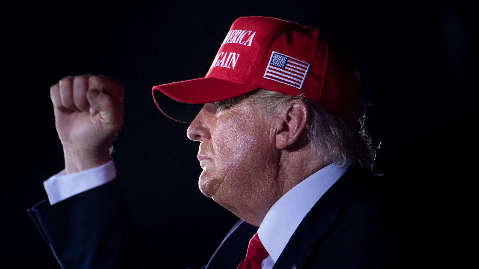 President Trump in profile, close up, in a red MAGA cap, pumping his fist.