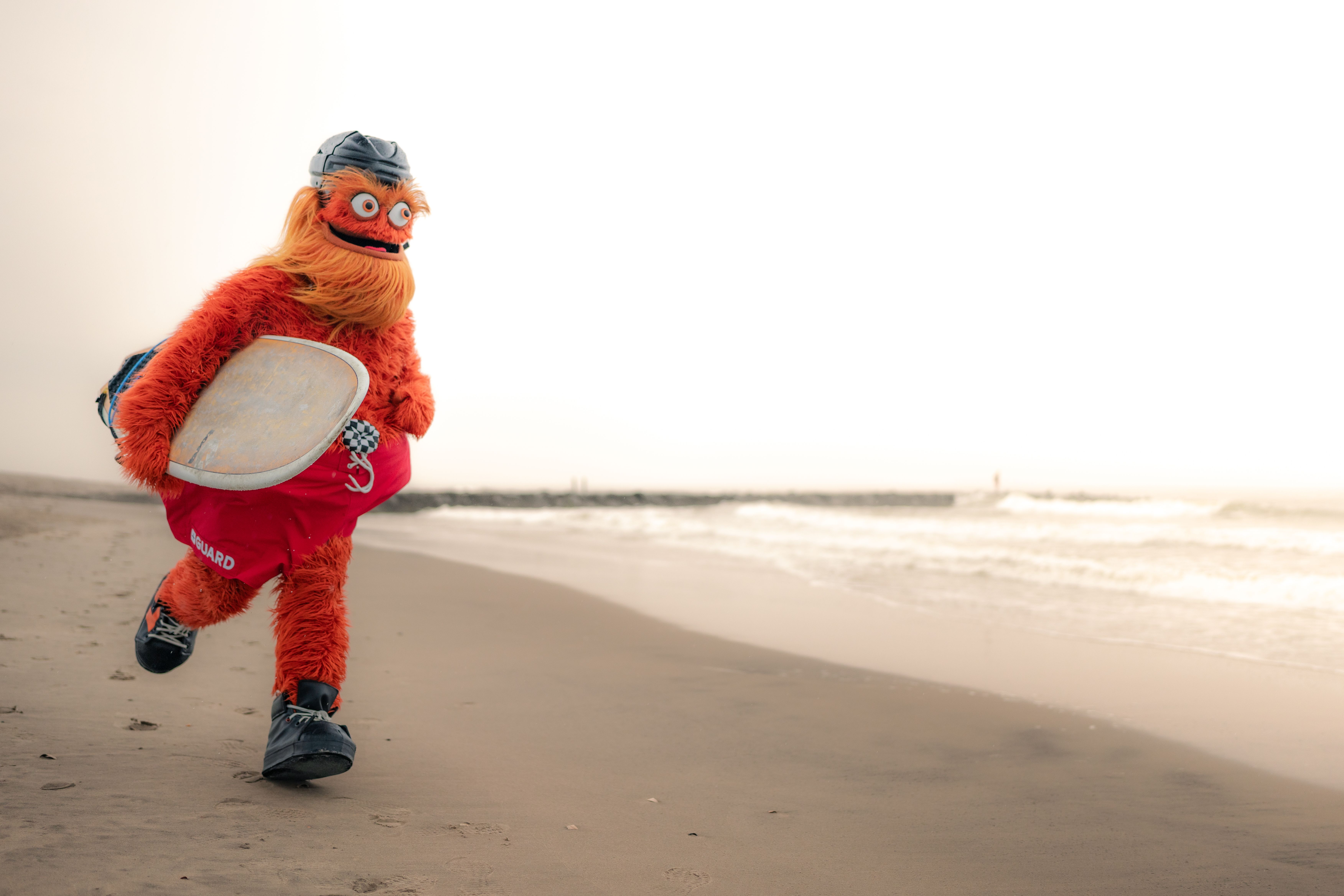 Gritty holding a surfboard while running on a beach. 