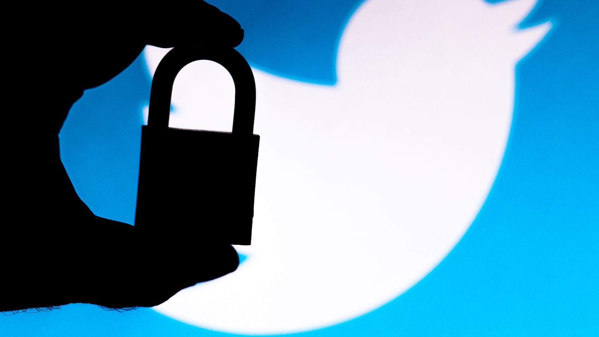 A photo illustration of a padlock in silhouette held in front of a large Twitter logo.