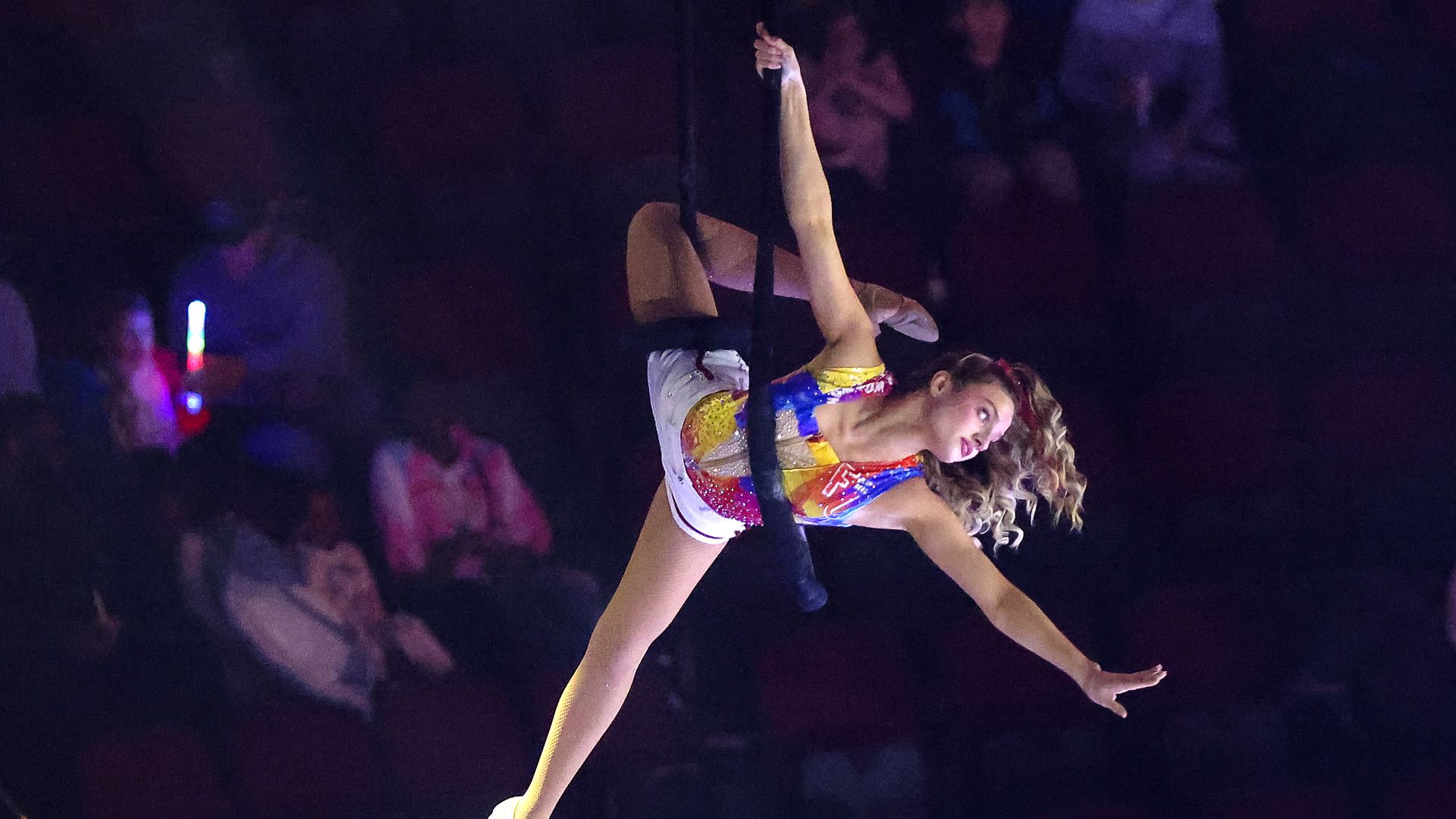 An aerial acrobat in a colorful suit does the splits in the air.