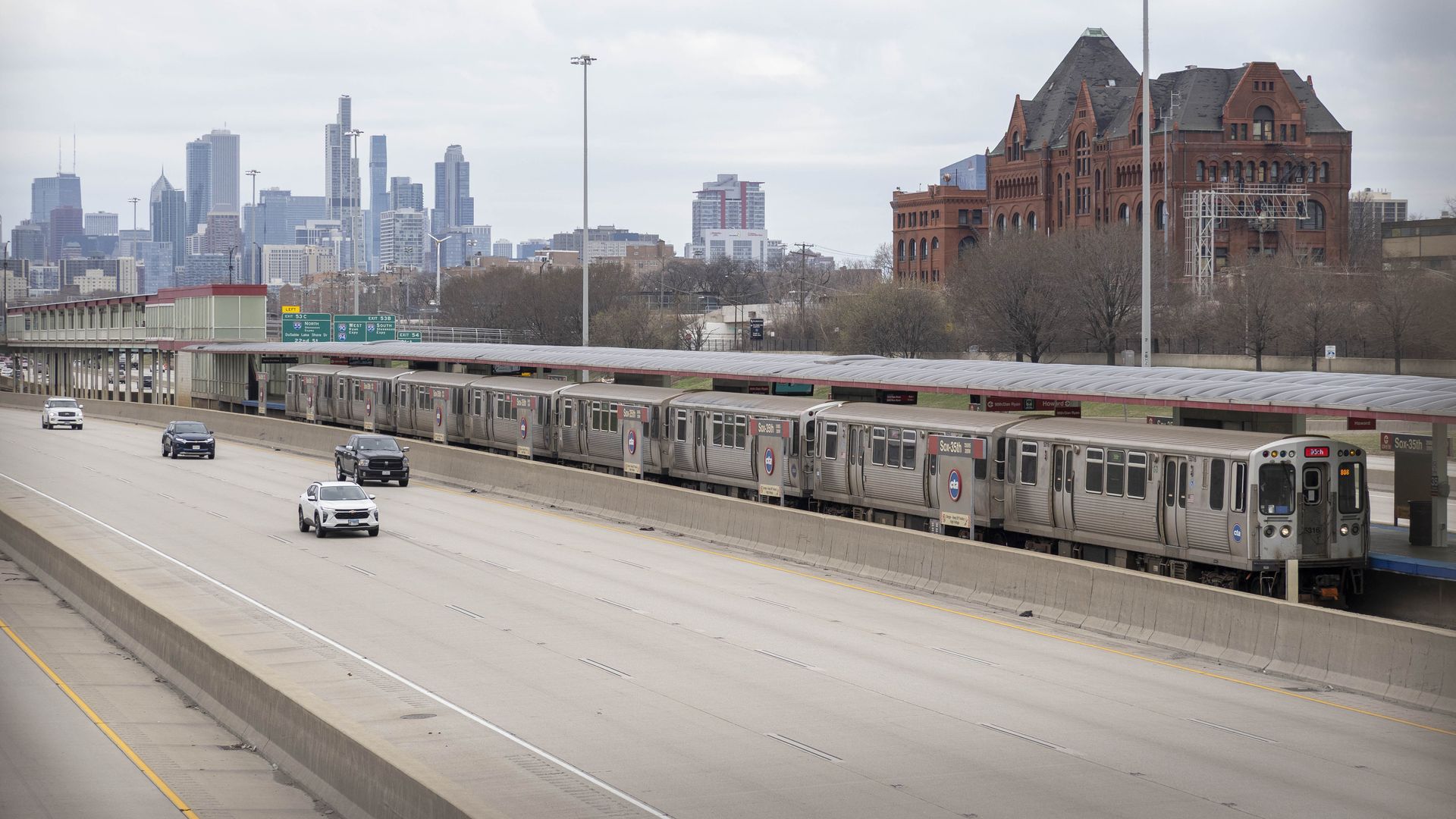A Chicago Transit Authority train alongside an expressway with Chicago's skyline in the background.