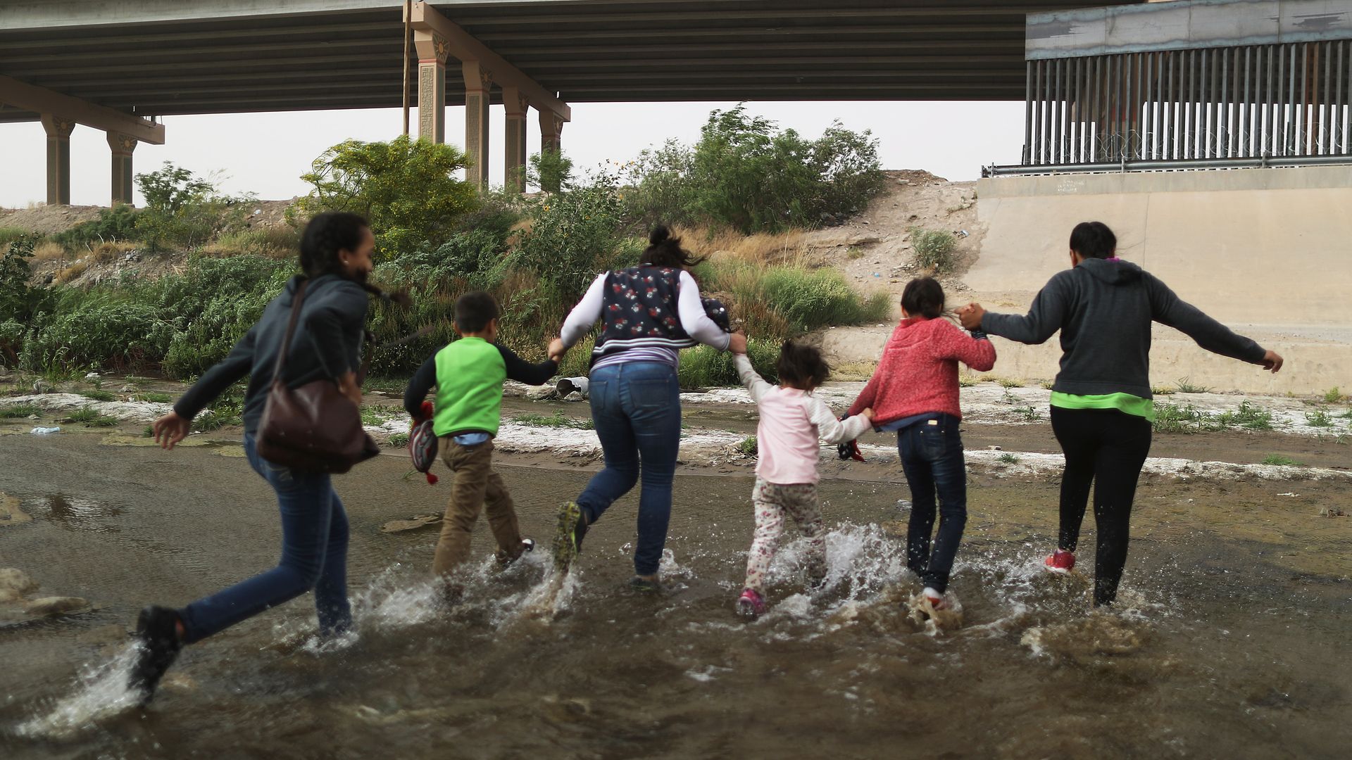 A group of 5 migrant women and young girls run through a puddle toward the U.S. border. 