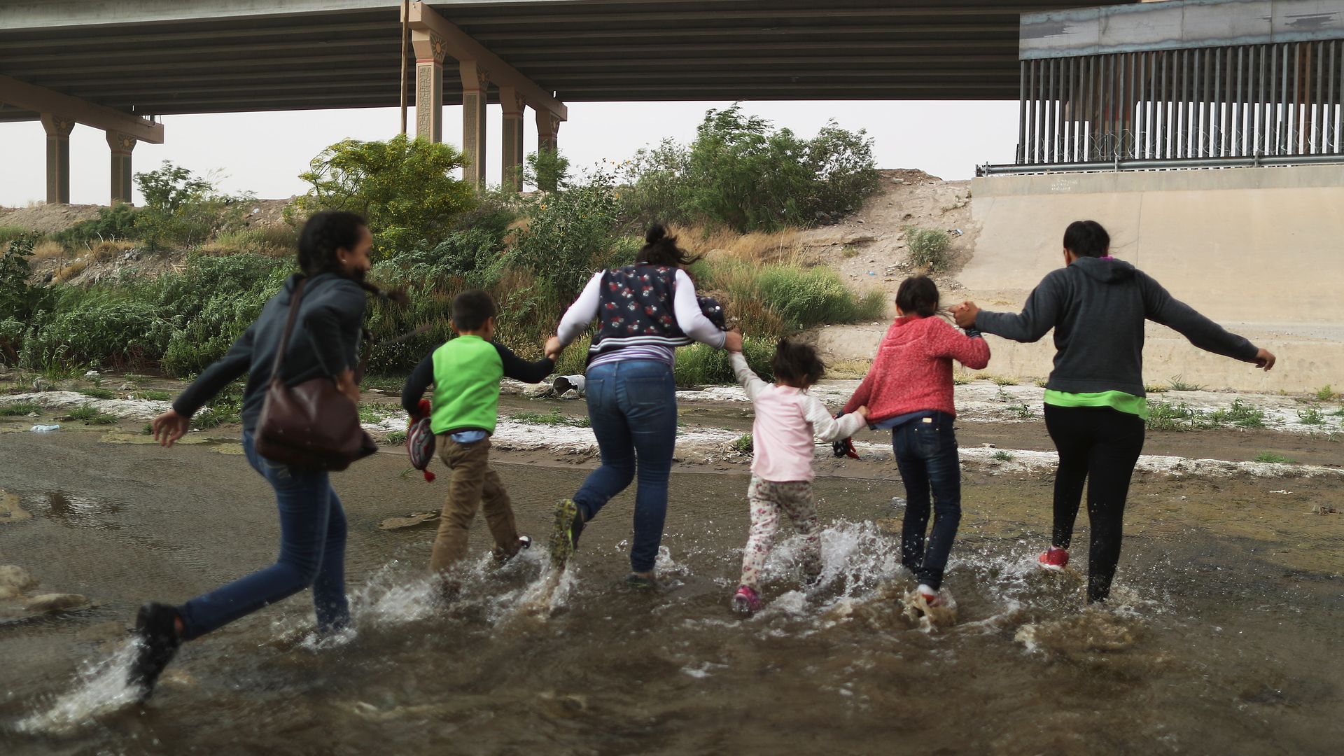 A group of 5 migrant women and young girls run through a puddle toward the U.S. border.
