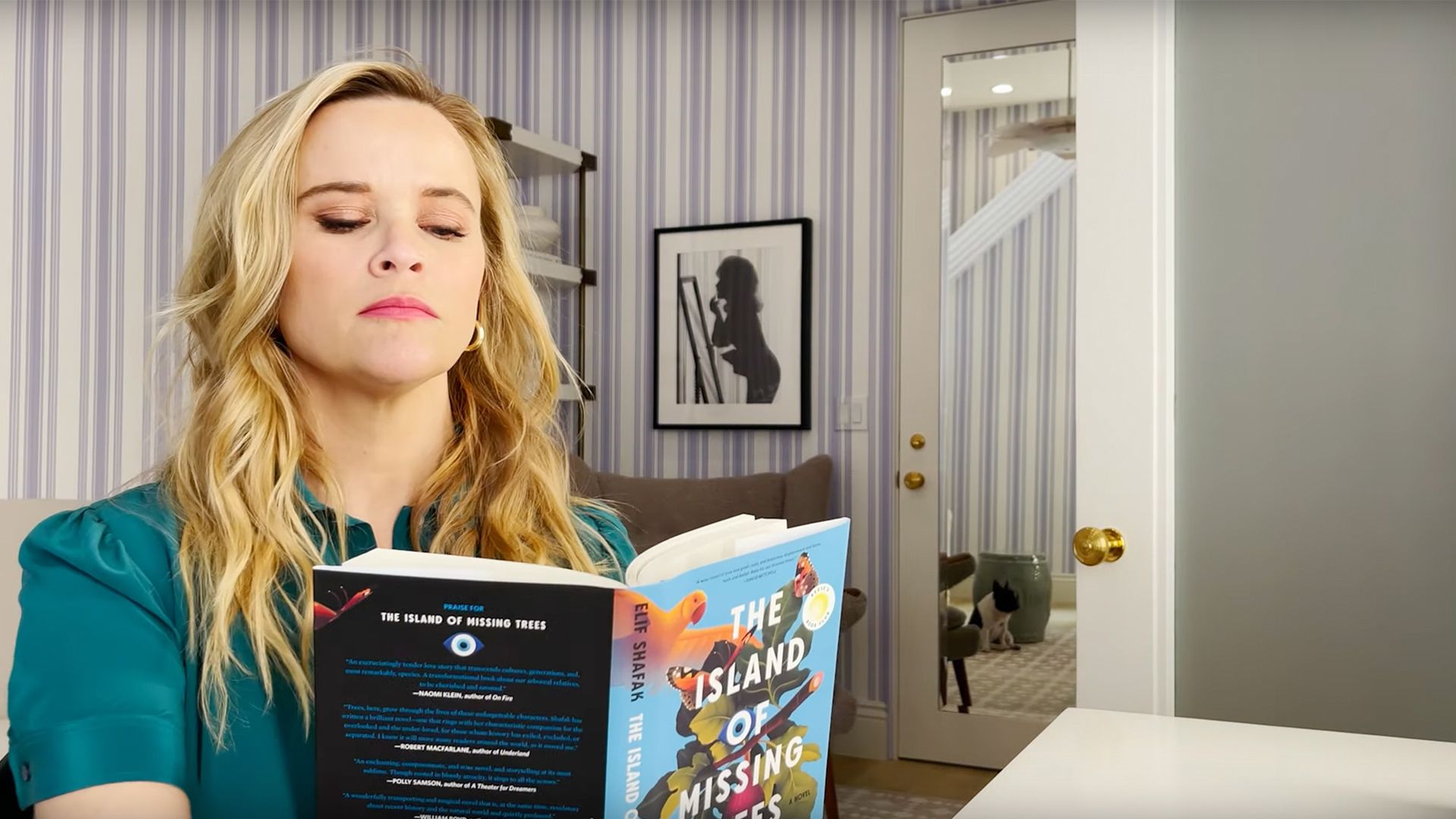 Photo of Reese Witherspoon sitting at a desk reading a book.