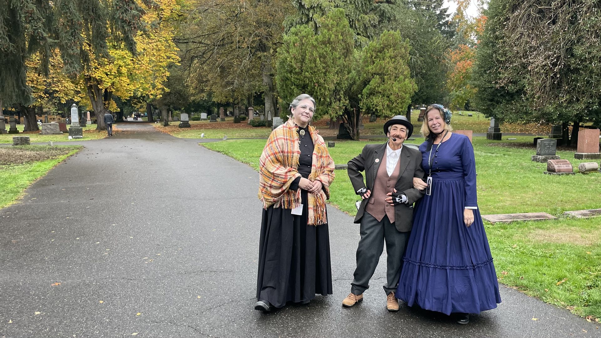 A photo of three people dressed up as ghosts standing in a cemetery.