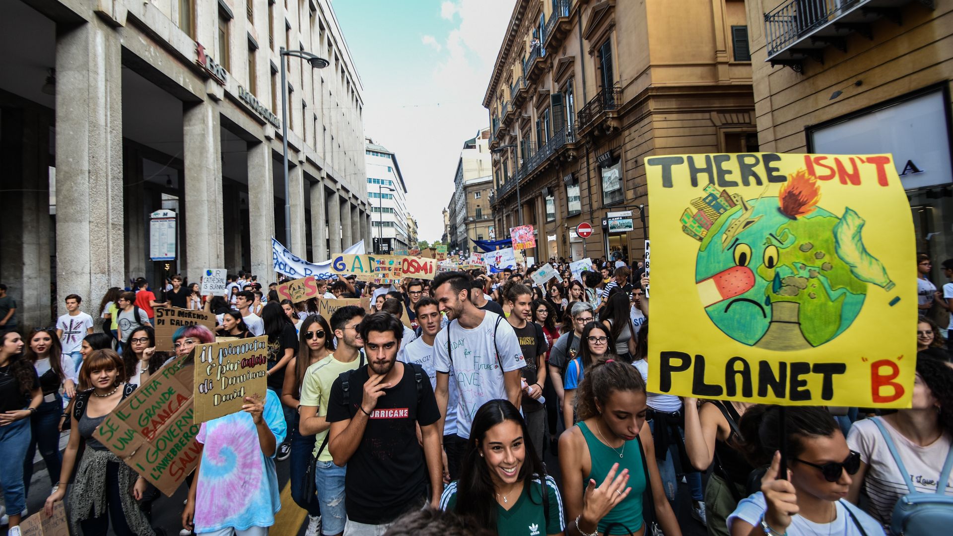 This image shows a long crowd of student protestors walking down a street in Italy with buildings on either side. A sign reads: "There is no Planet B" 
