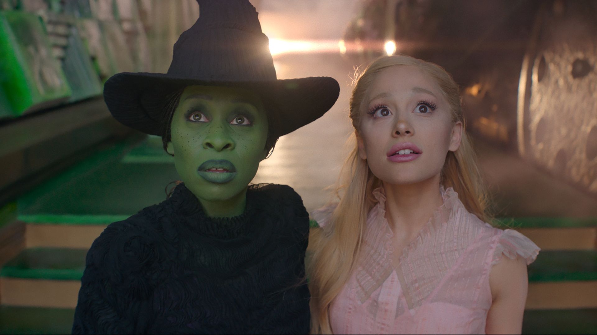 Cynthia Erivo is Elphaba (wearing black and has green skin) and Ariana Grande is Glinda is wearing pick in photo from Wicked movie
