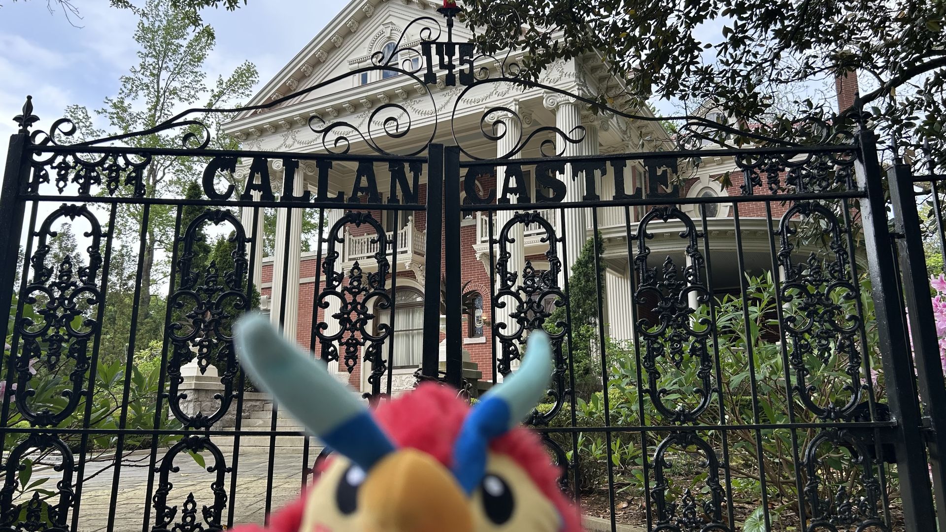 A stuffed toy animal Phoenix is blurry in the foreground of a photo of a wrought-iron gate with the words "Callan Castle"
