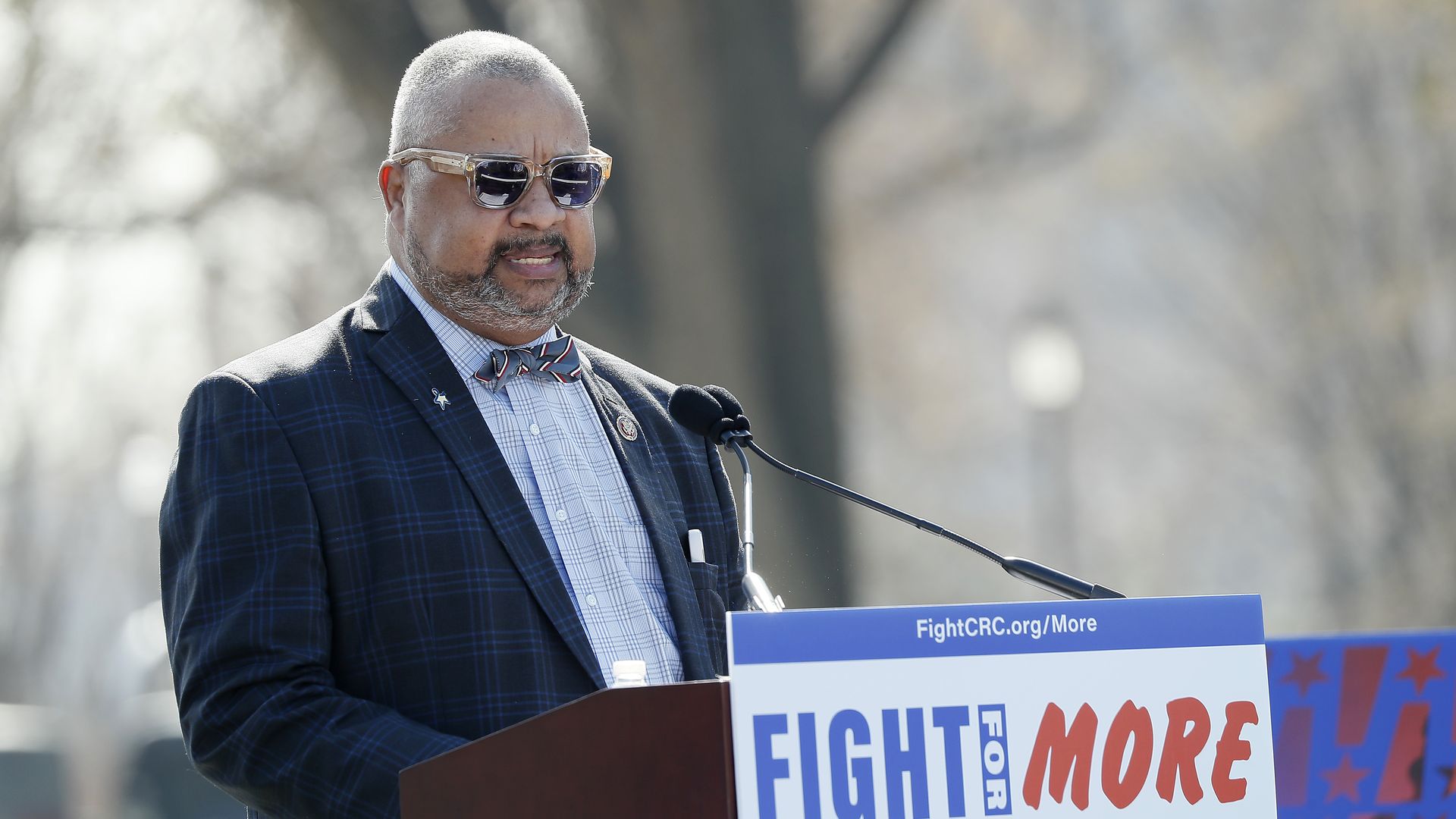Rep. Donald Payne Jr., wearing a blue suit, bowtie and sunglasses, speaking at a podium outside.
