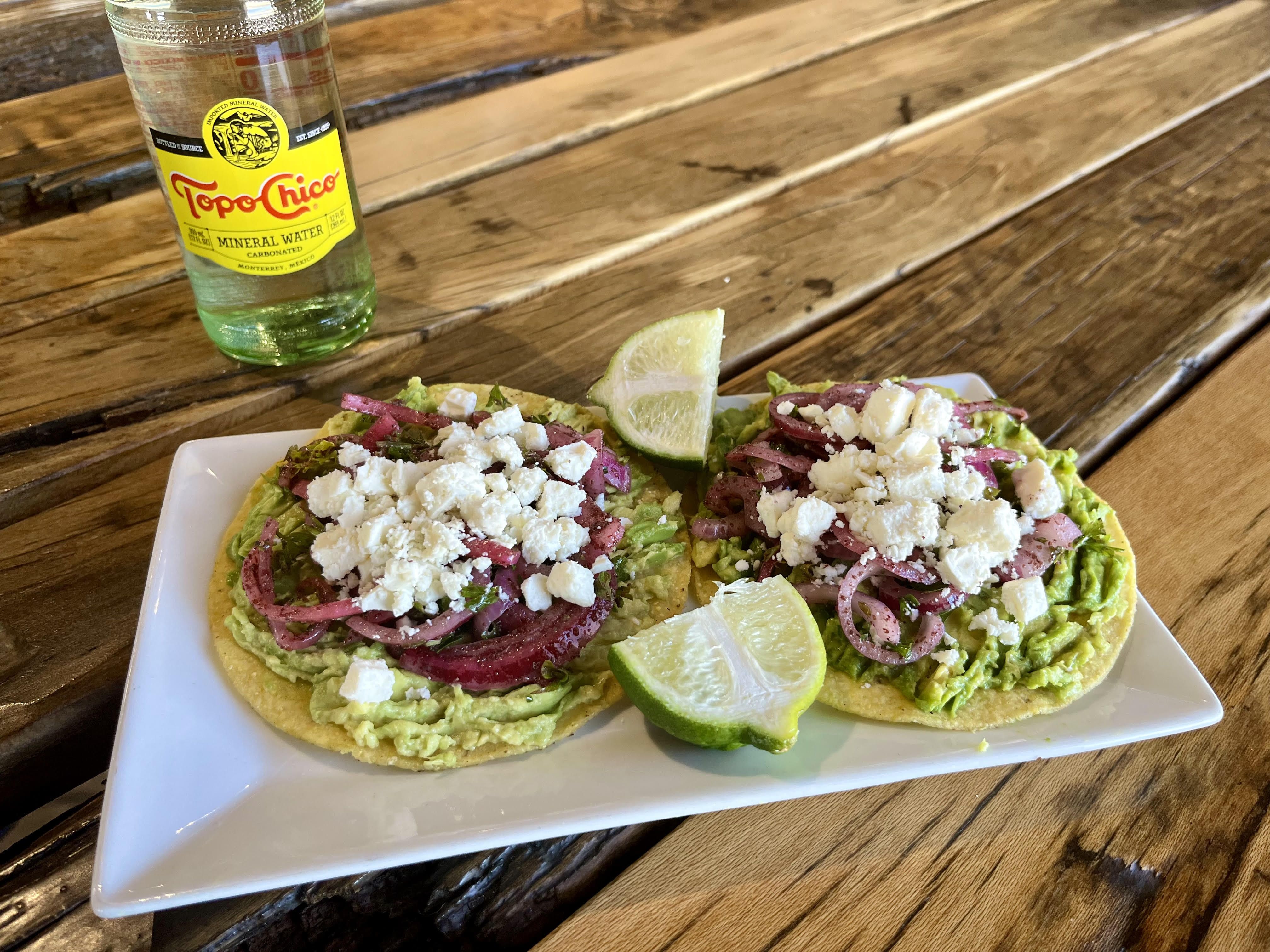 A Topo Chico bottle and a plate of tostadas on a wooden table. 