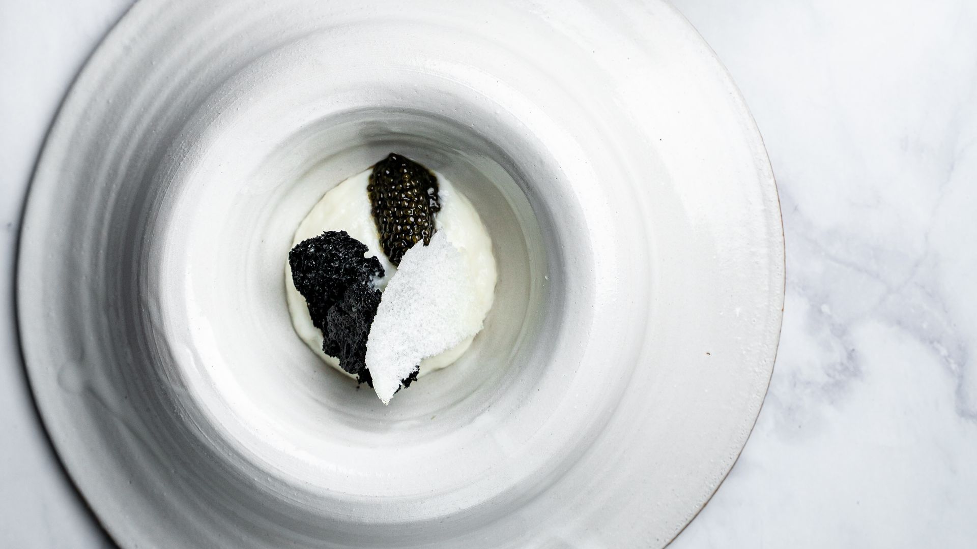 caviar sits on a white plate on a marble table. 