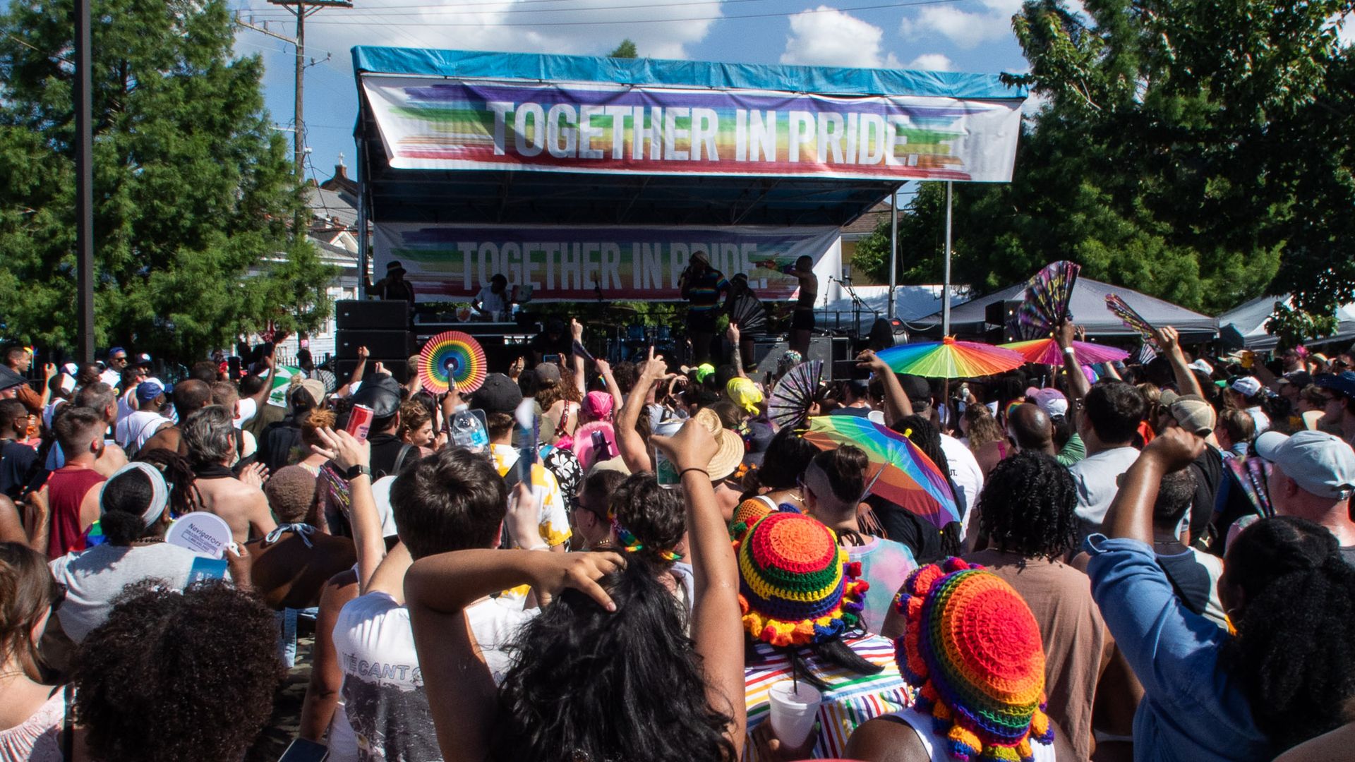 Image shows people in front of a stage that says "Together in Pride"
