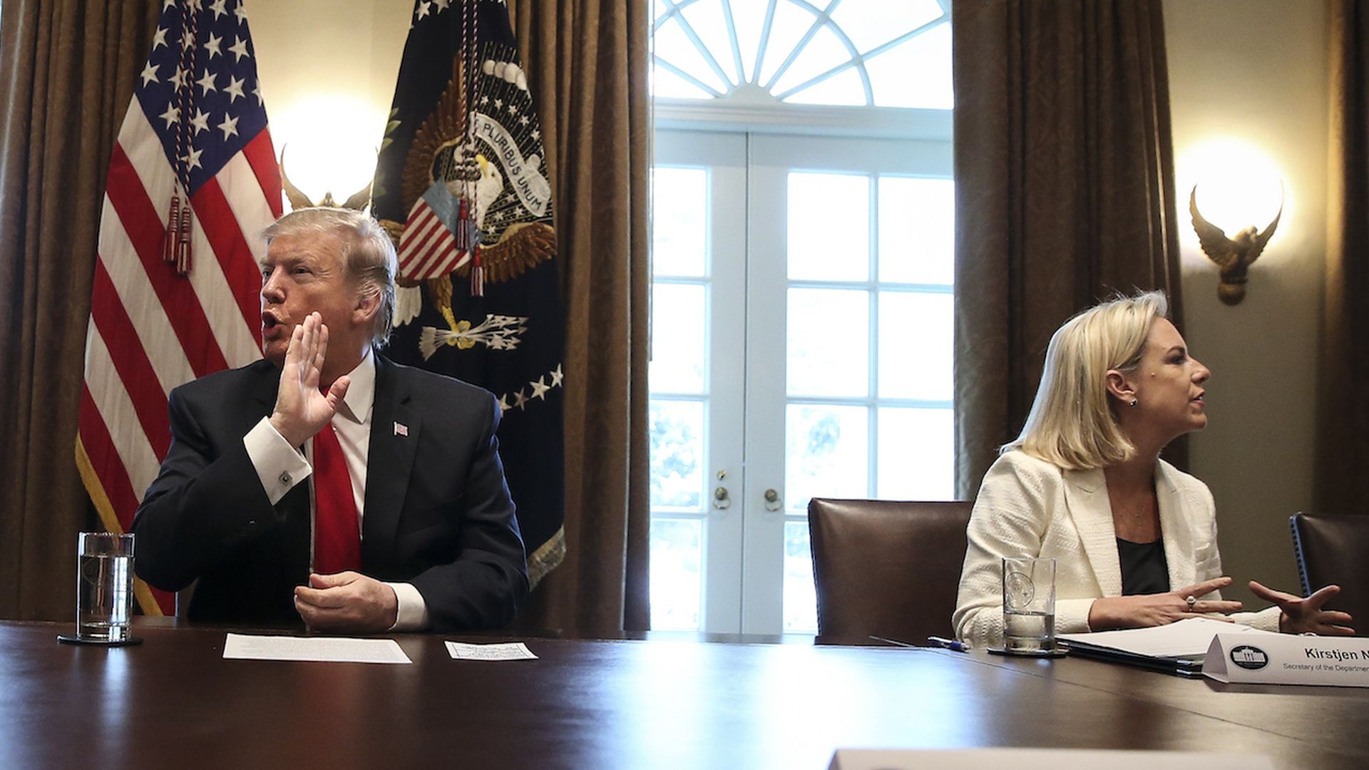 Donald Trump and Kirstjen Nielsen looking in opposite directions, with a table in the foreground