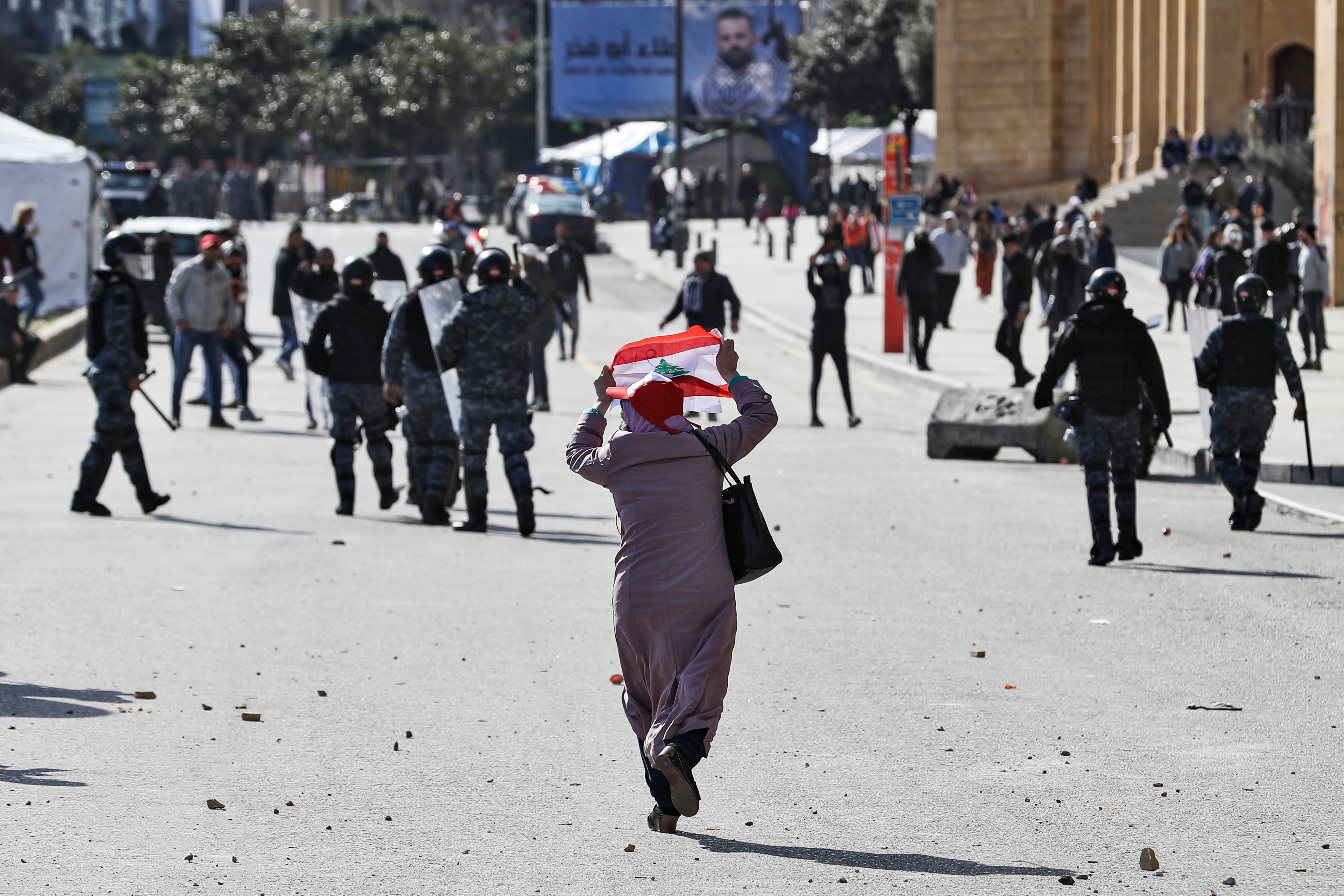 Elderly woman holding a Lebanese flag behind anti-riot police