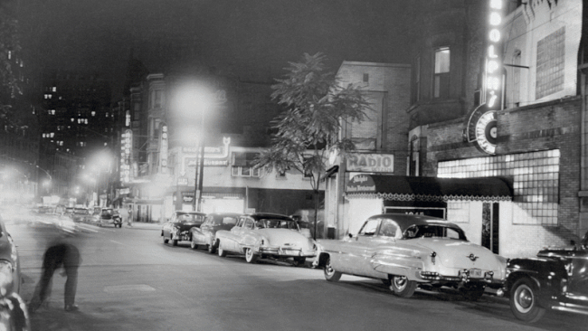 Photo with old automobiles lining streets fades into new photo of today. 