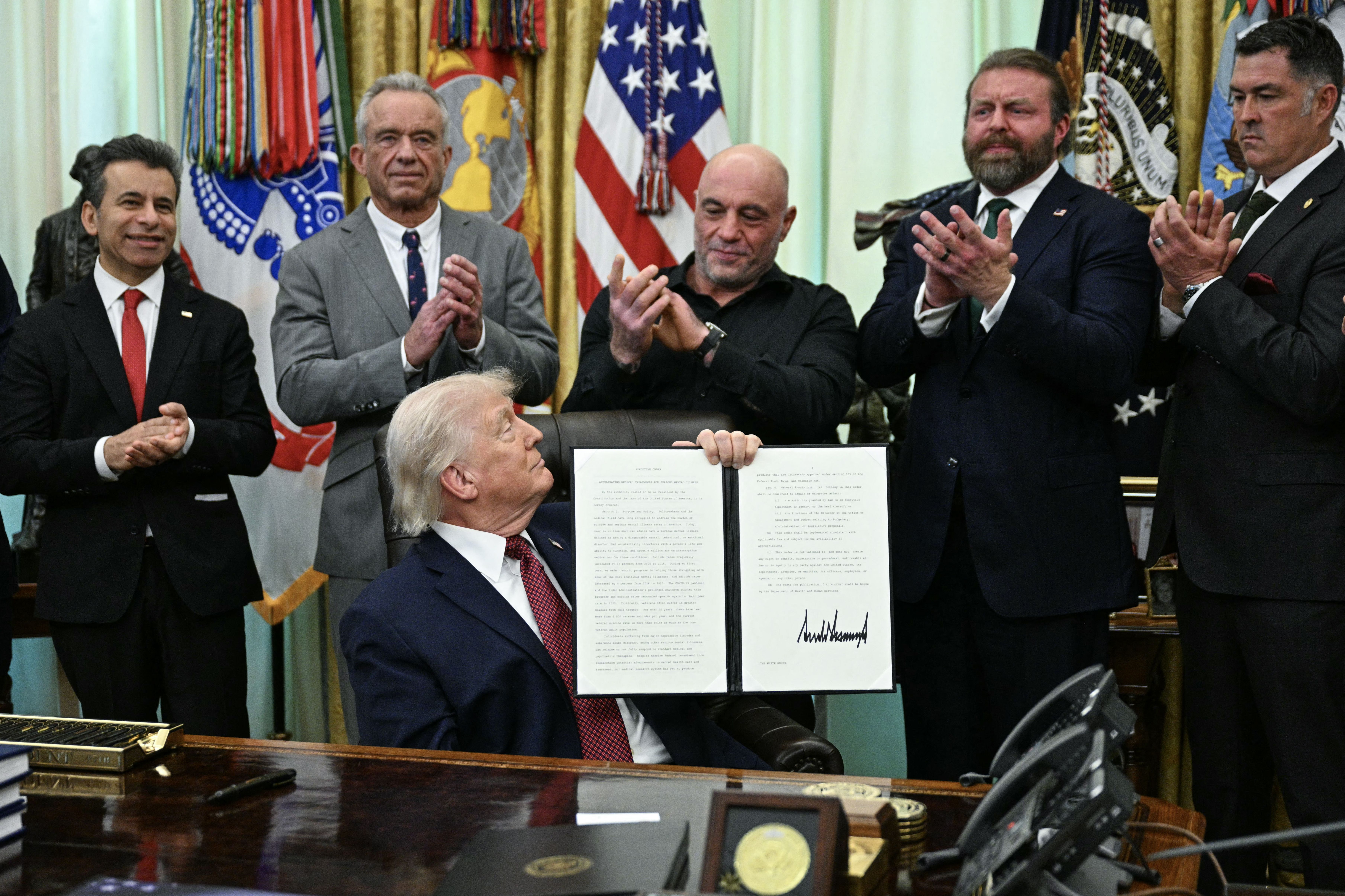 (L/R) FDA Commissioner Marty Makary, Health and Human Services Secretary Robert F. Kennedy Jr., US media personality Joe Rogan, W. Bryan Hubbard, CEO of Americans for Ibogaine, and former Navy SEAL Marcus Lutrell applaud after US President Donald Trump signed an executive order in the Oval Office of