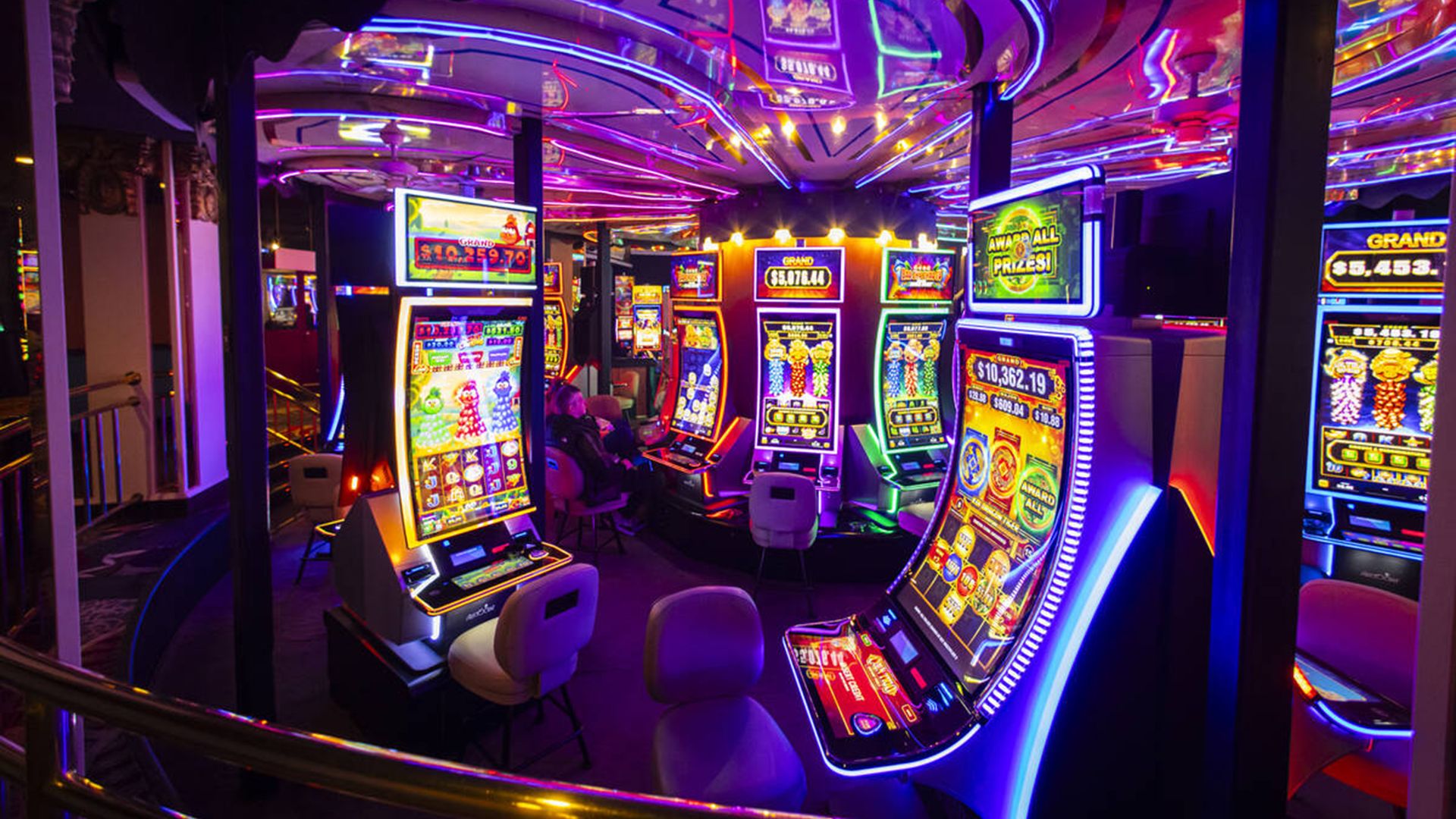 Colorful casino slot machines with bright neon lights in purple, pink, blue, and yellow hues creating a vibrant, reflective ceiling atmosphere