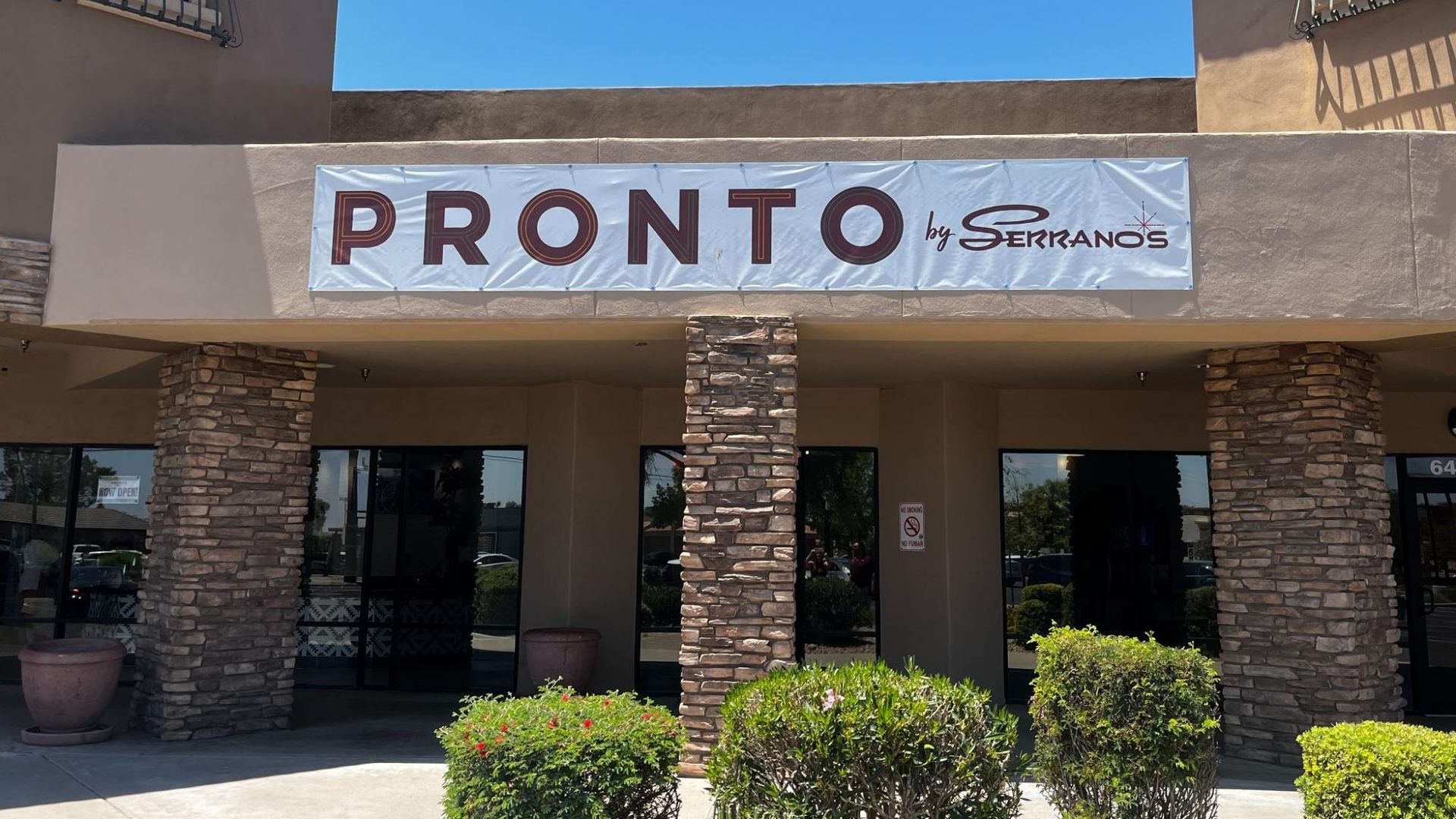 A building entrance with brick support pillars and a sign that reads Pronto by Serrano's.