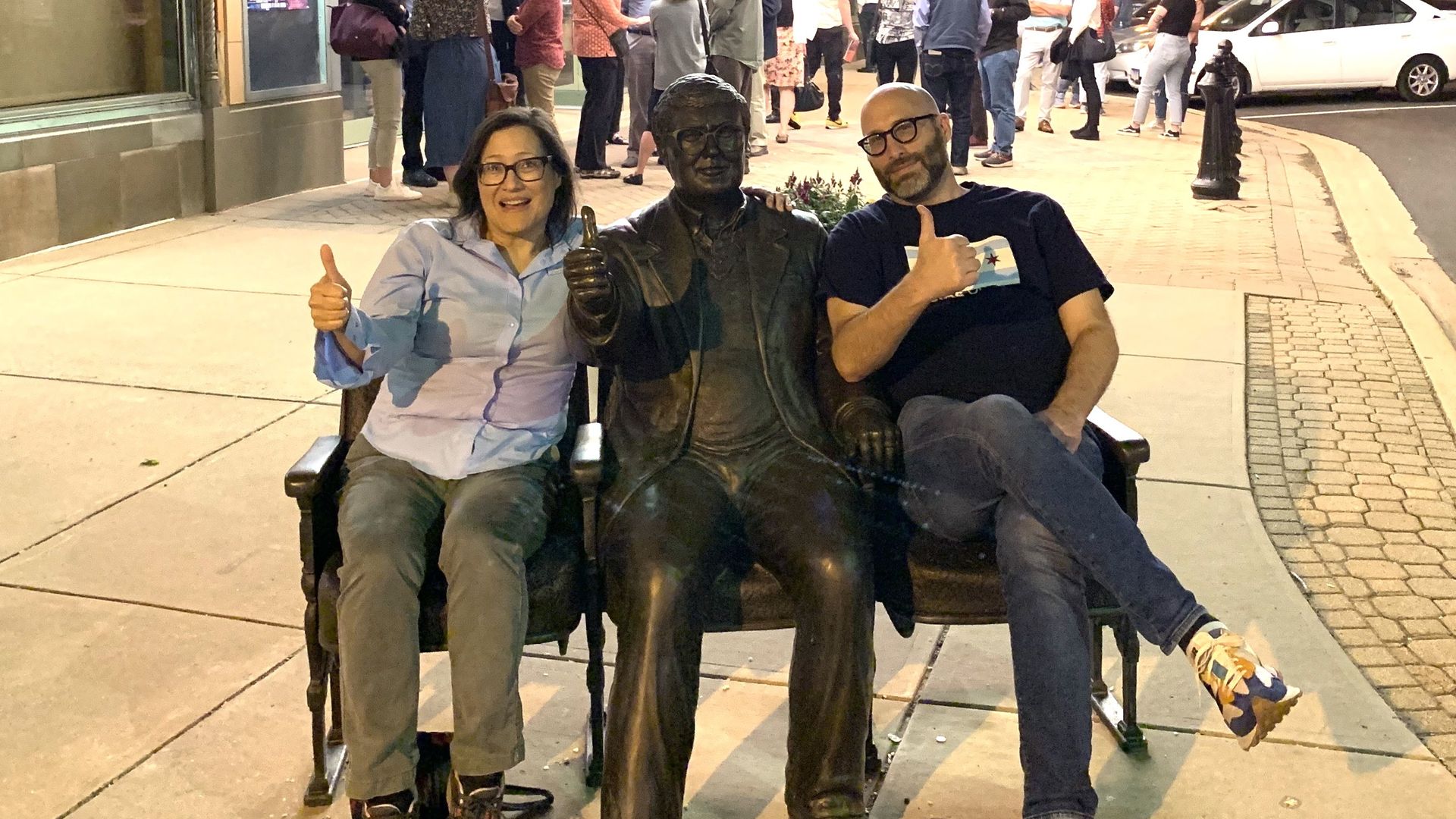 Photo of two people sitting with a statue. 