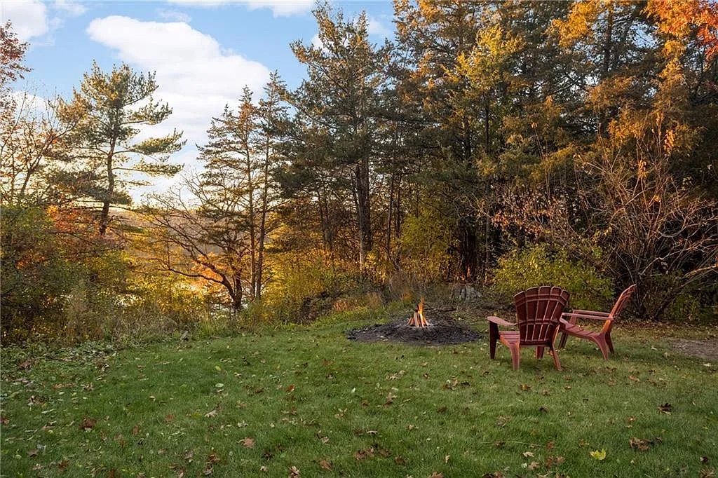 Two red wooden chairs around a fire pit overlooking a wooded area with green and red trees.