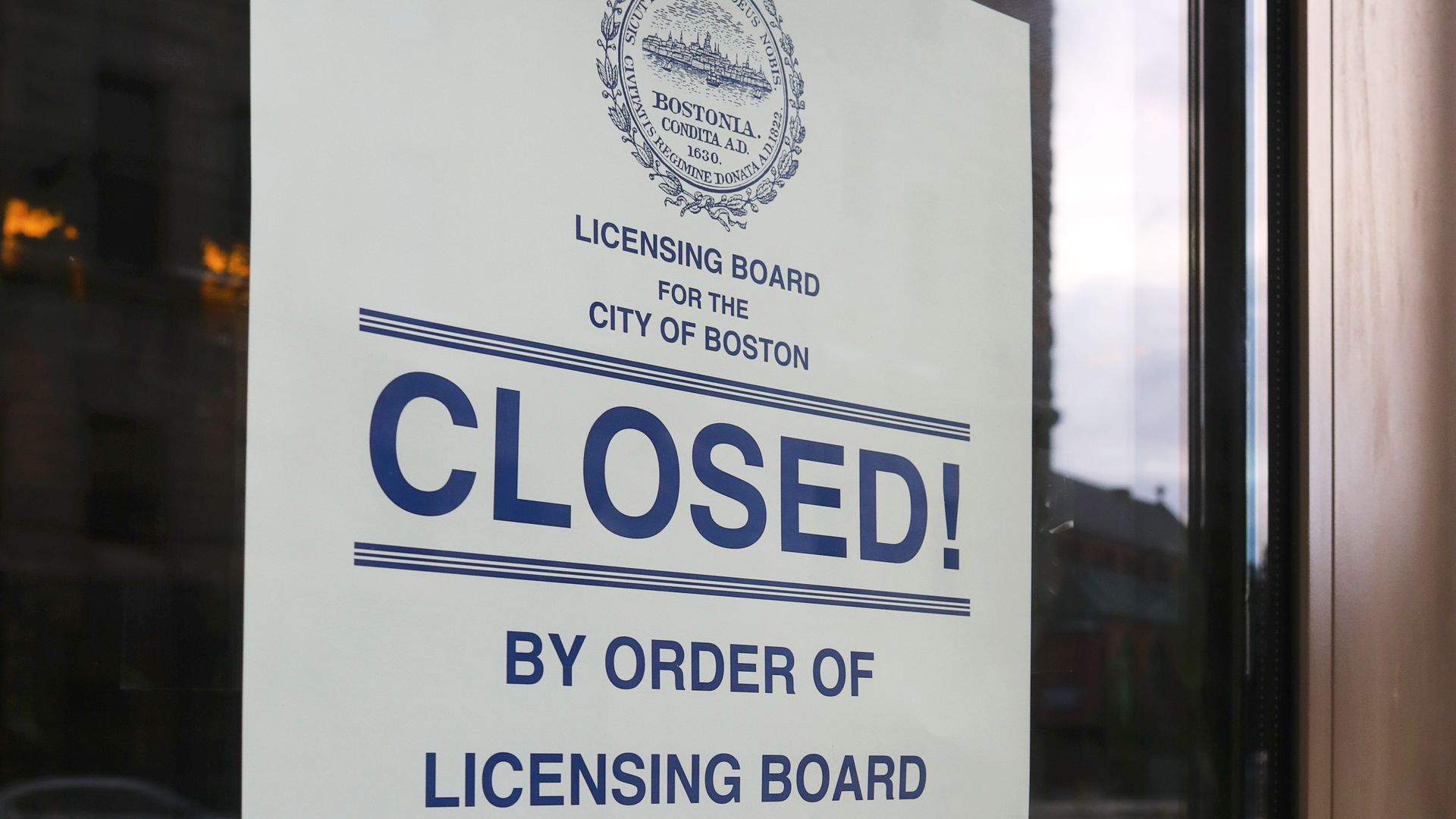Official white sign on a glass door with blue text stating "CLOSED! By order of Licensing Board for the City of Boston" with a city seal and names of board members at bottom.