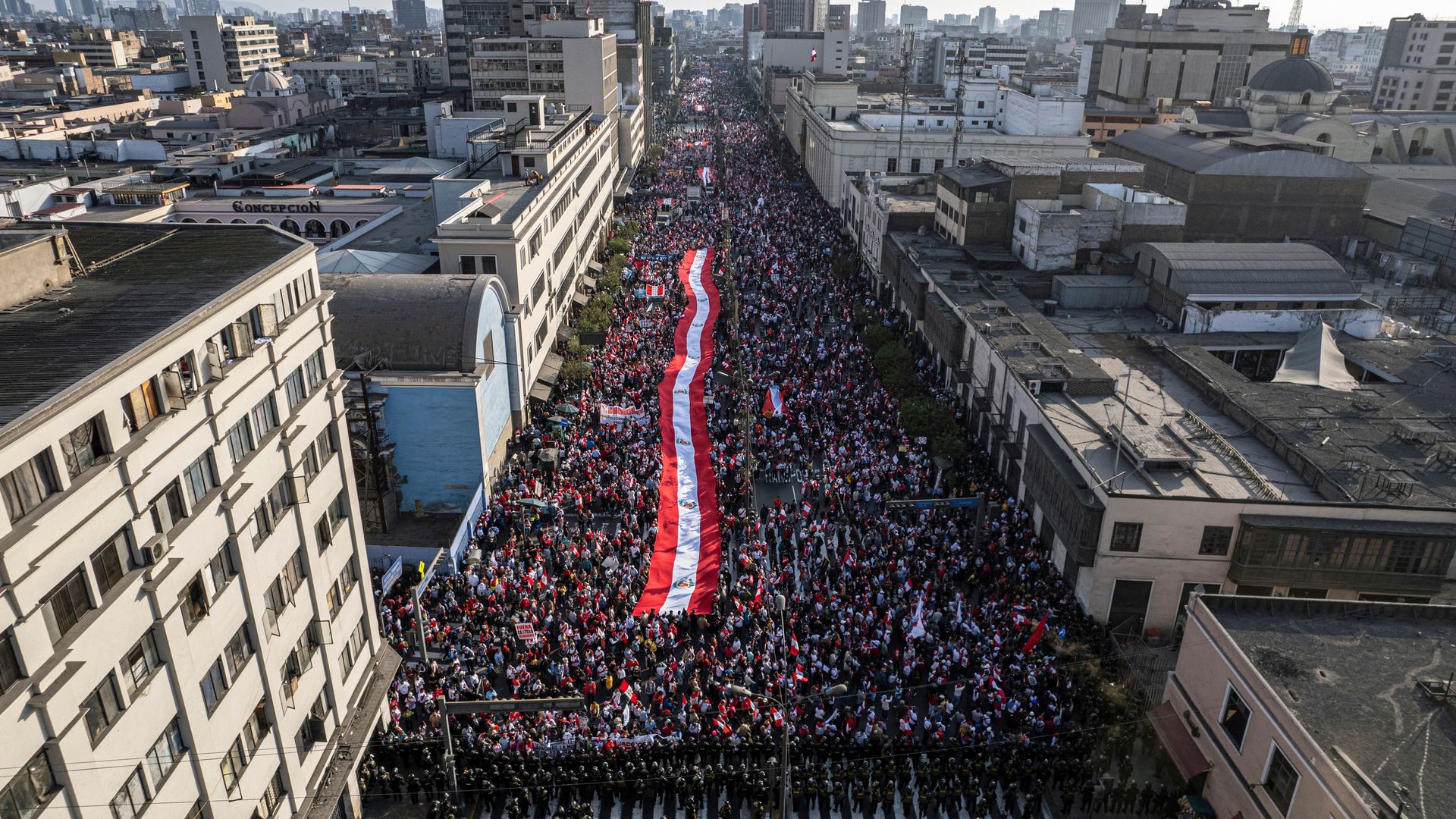 A large crowd of protesters is seen walking through a Peruvian street