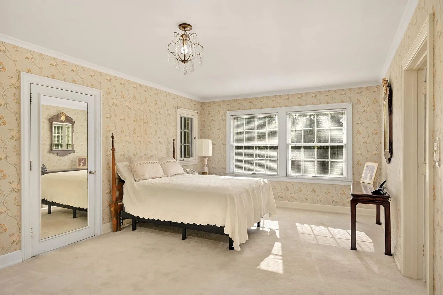 A bedroom with a white bed, white carpet and floral wallpaper.