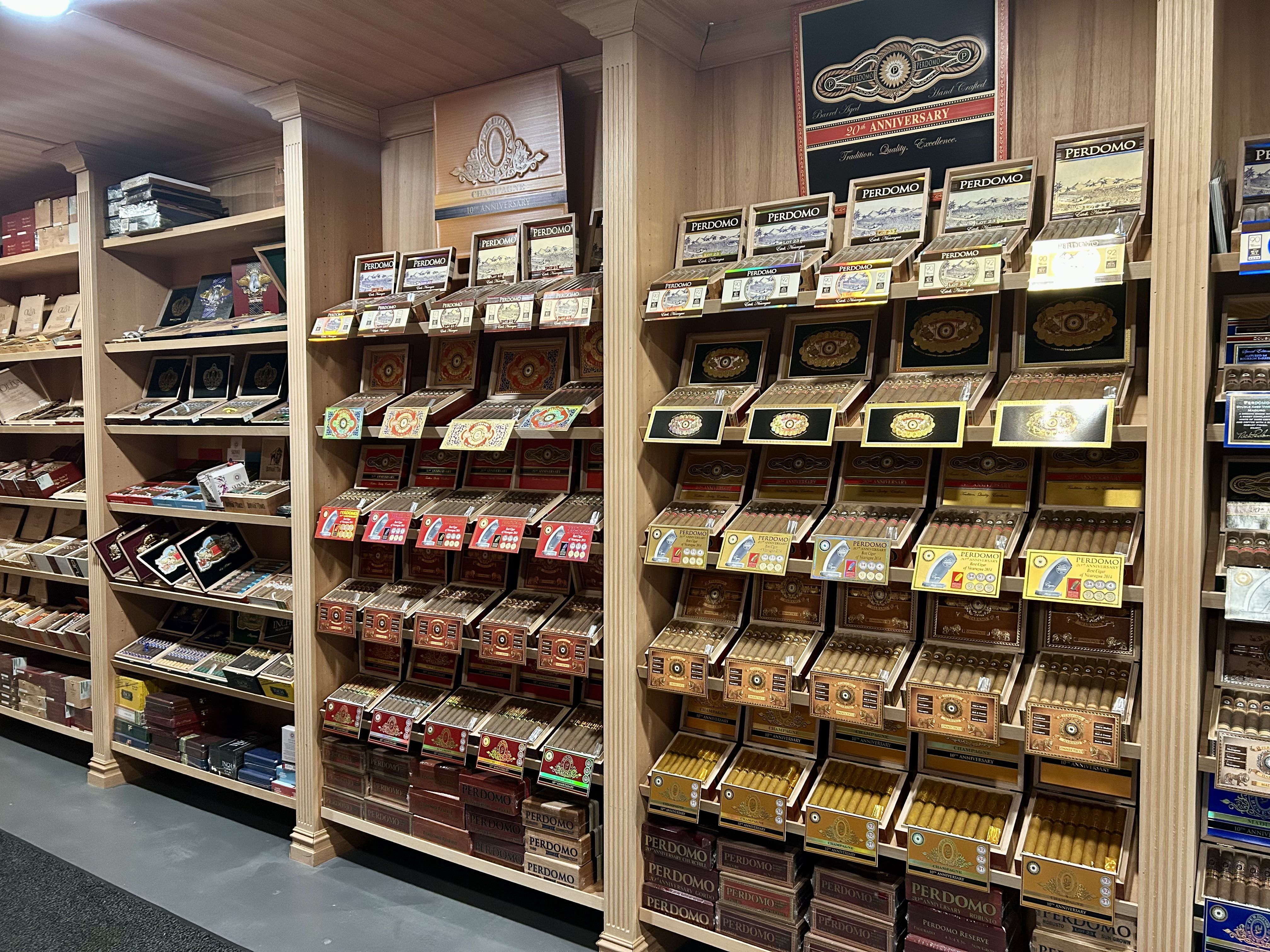 Iron oak cigar. Wide view of a wooden cigar shop display with many Perdomo cigar boxes on shelves. Brown, gold, and blue packaging, posters overhead, showcasing the Perdomo brand.