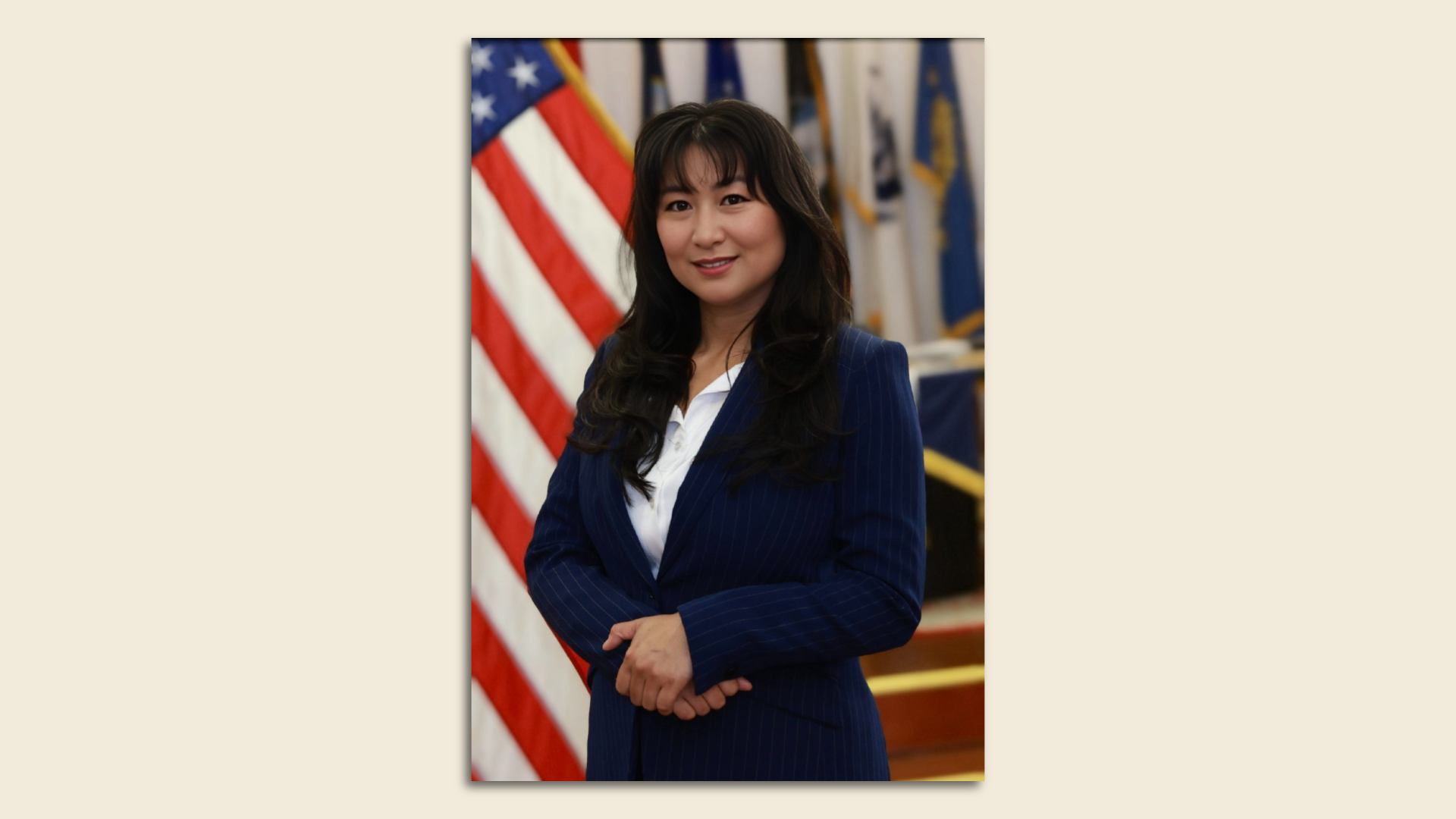Photo of Wendy Ha Chau in a dark navy suit standing in front of an American flag
