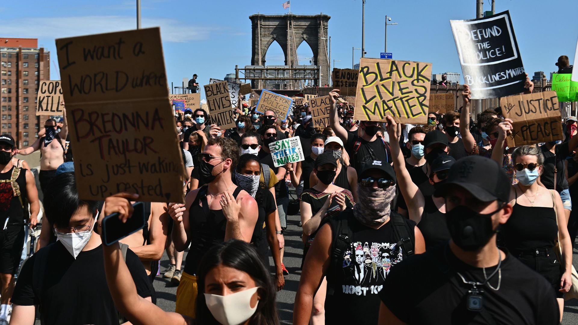 In this image, a crowd of protesters march. One sign reads "Black Lives Matter"