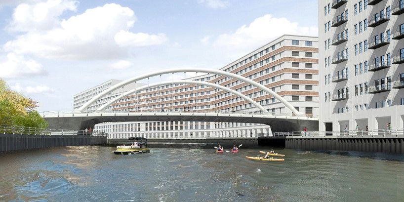 River scene with kayakers and a motorboat under a large white arched bridge, flanked by modern multi-story buildings under a partly cloudy sky.