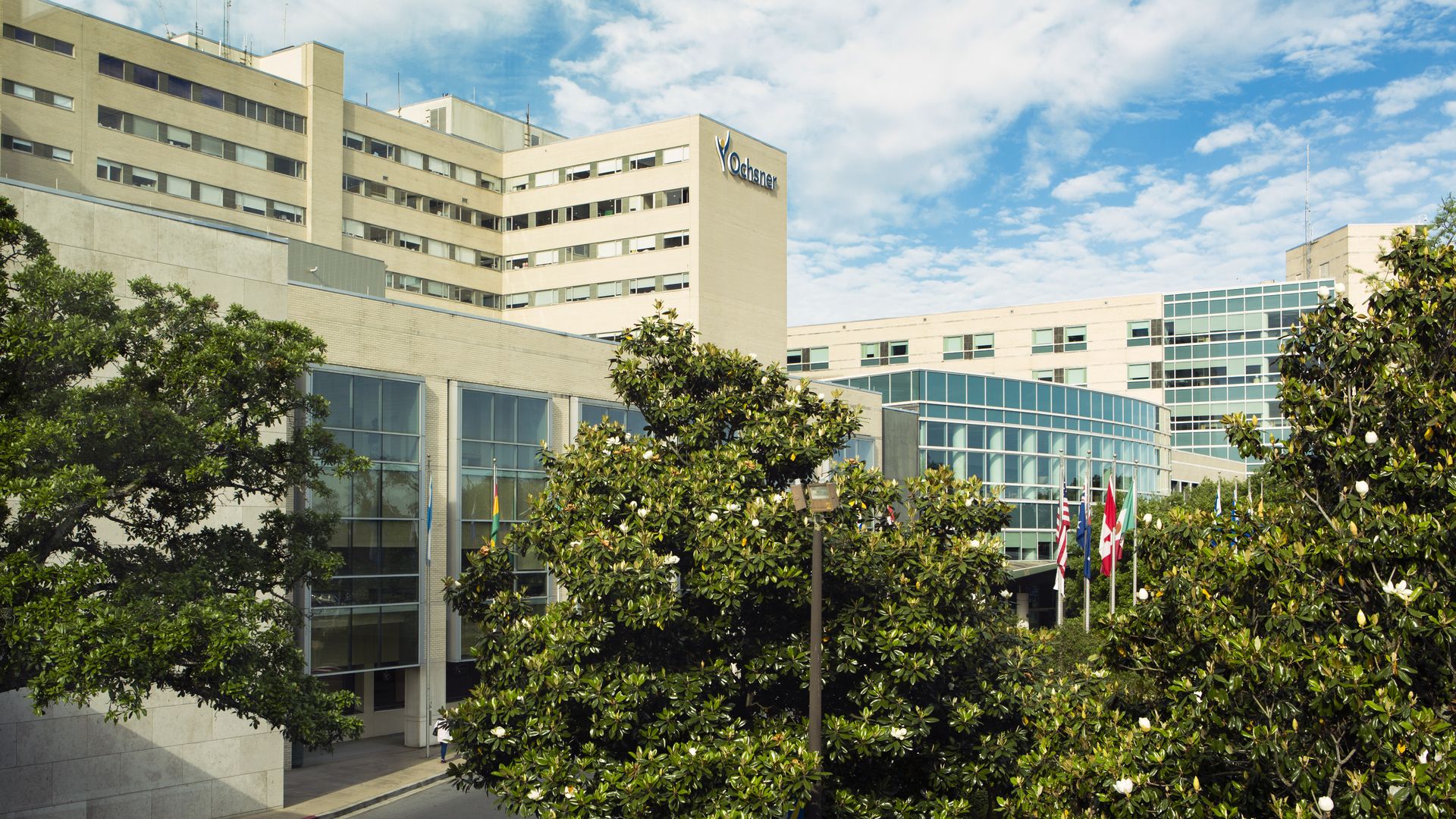 Photo shows an exterior view of Ochsner Medical Center in Jefferson Parish. Blooming magnolia trees are in the foreground.